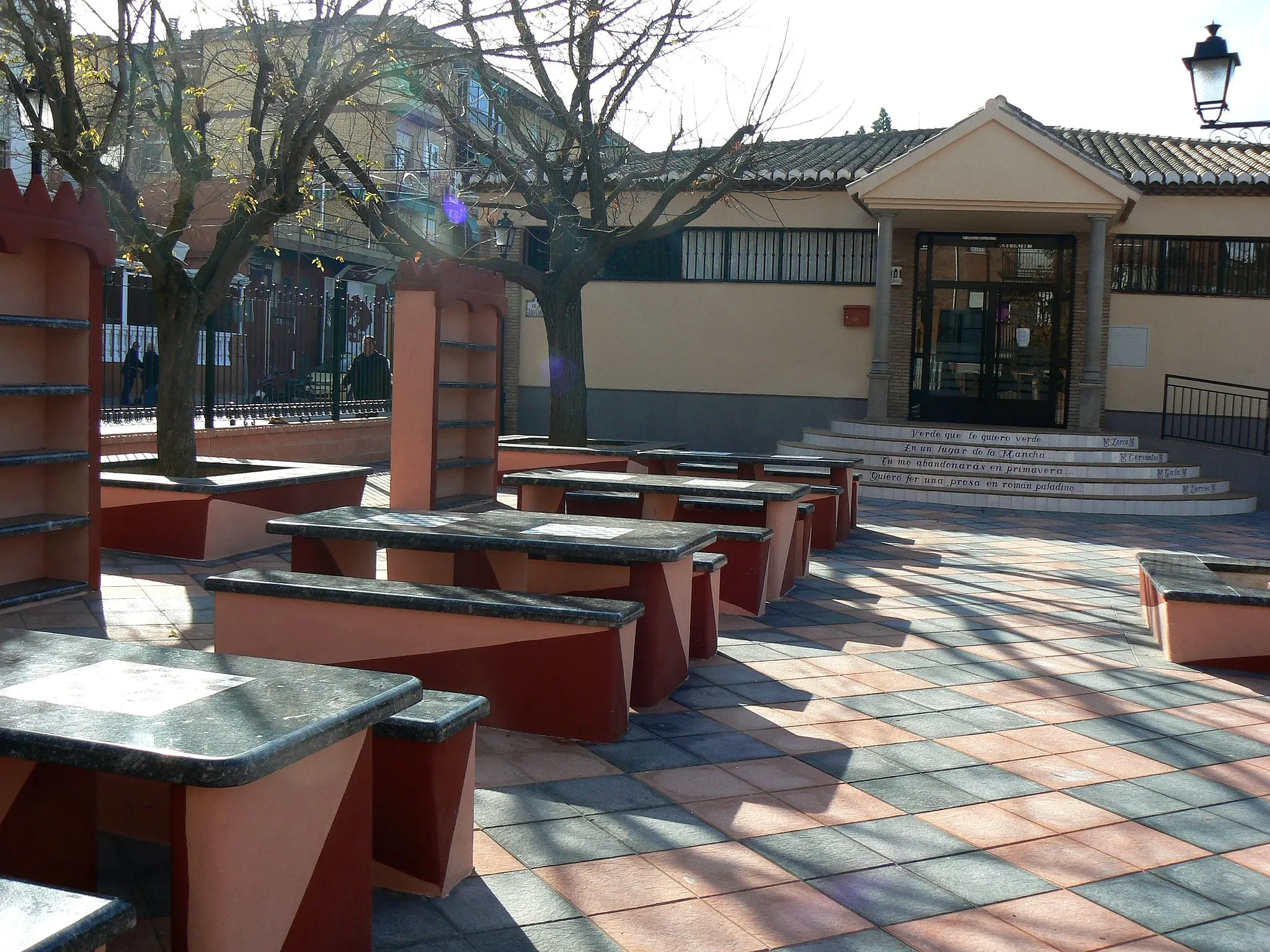 Photo showing: La biblioteca de La Zubia tras la remodelación llevada a cabo un año antes de la toma de la foto. Desde entonces, la iglesia se encuentra dentro del Parque de La Encina y no colindante, por lo que no se puede acceder al área mostrada en la fotografía si el parque se encuentra cerrado. En las escaleras de la entrada hay versos de famosos poemas. En los armarios exteriores hay libros que cualquiera dentro del parque puede tomar y leer en cualquier momento.