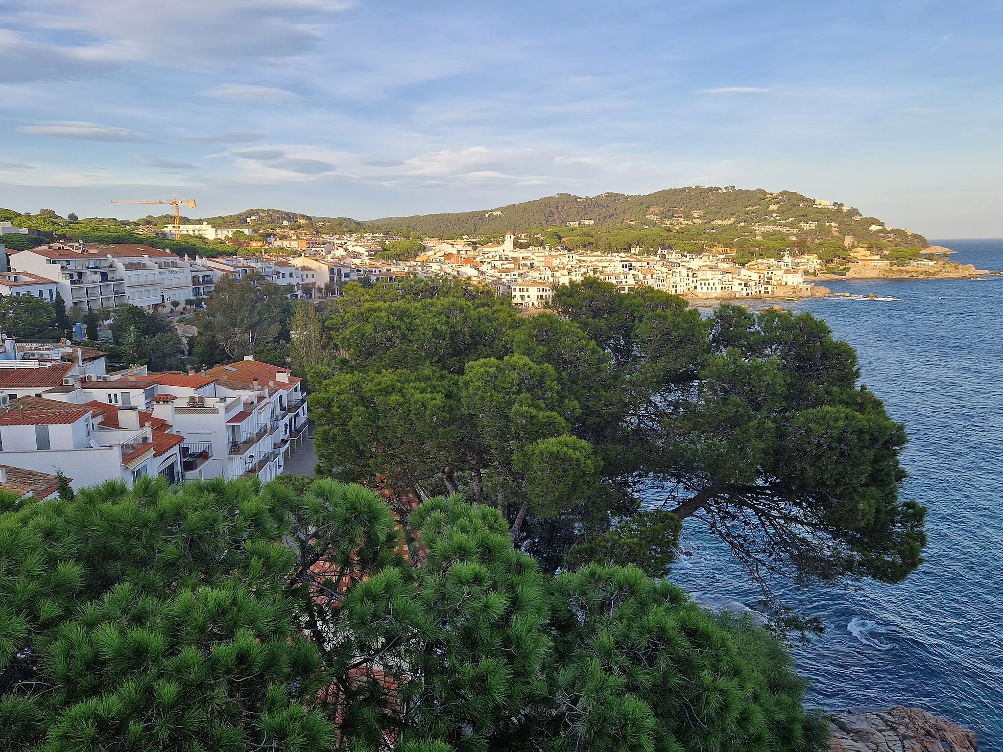 Photo showing: View of Calella de Palafrugell, Catalonia, Spain. The second headland (with the watch tower) hides the next resort of Llafranc, but the lighthouse of Sant Sebastià (beyond LLafranc) can be seen on the furthest headland. Photograph taken from the Hotel Sant Roc. The same view by night can be seen here.