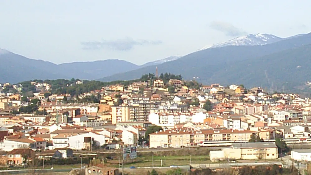 Photo showing: El Turó del Puig de Bellver és el cim en primer terme que està coronat per un campanar. A sota està la ciutat de Sant Celoni i al fons el massís del Montseny