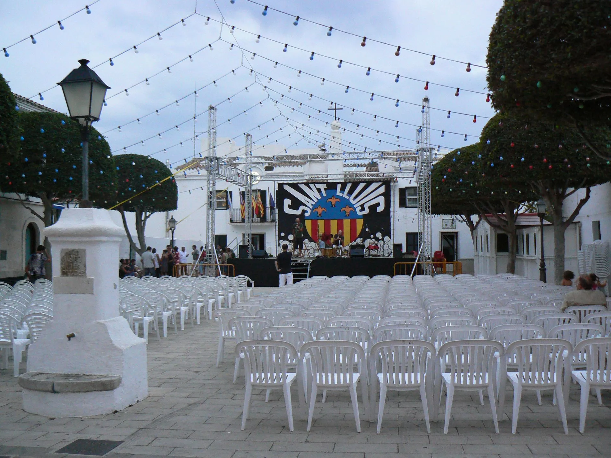 Photo showing: El pla de sa Creu amb l'ajuntament al fons, a l'esquerra, preparant-se per a les festes majors de Sant Lluís (Menorca), que es celebren el dia 25 d'agost. Vista des de l'esglèsia de Sant Lluís.