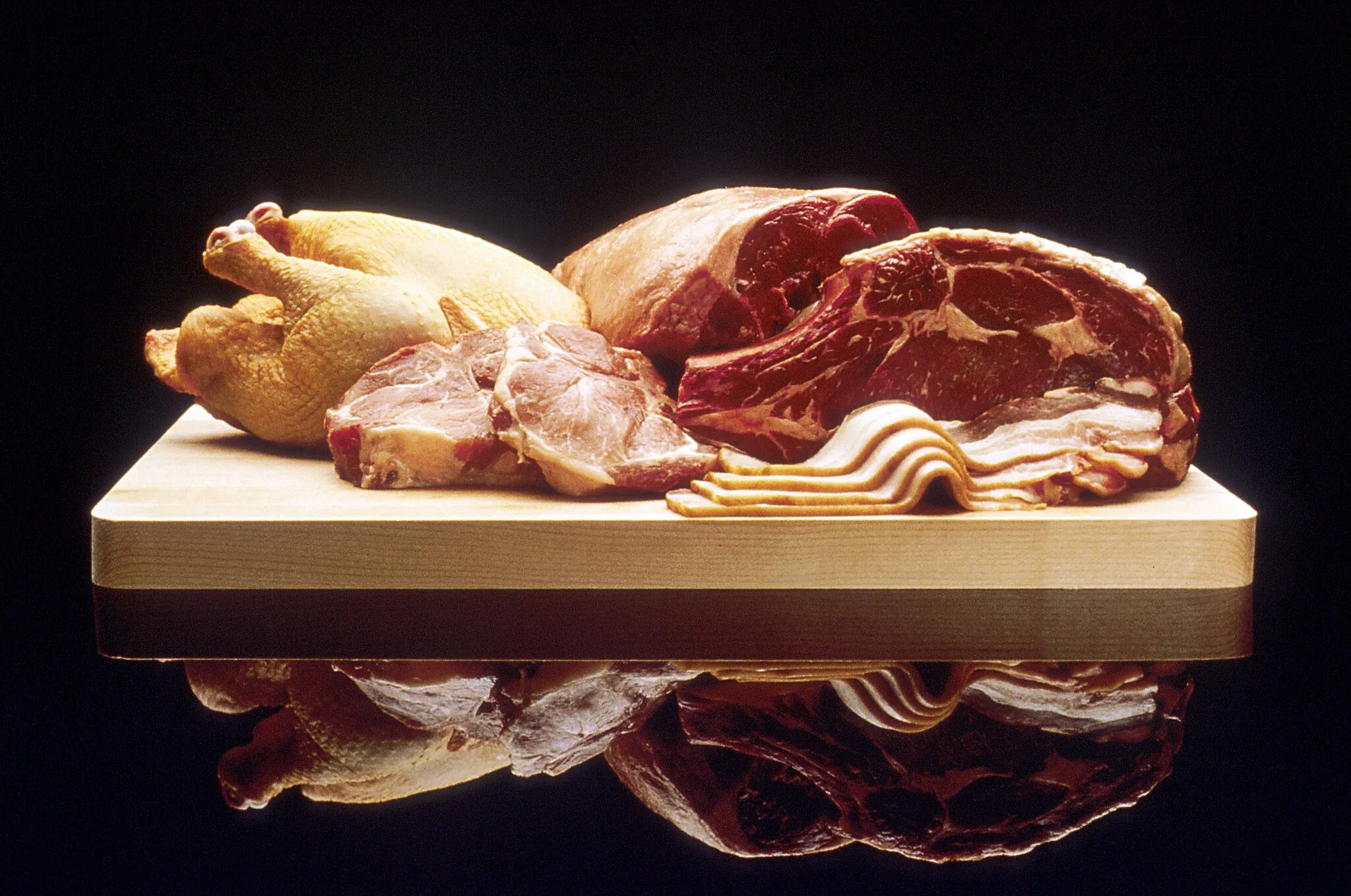Photo showing: Display of red meat (right), poultry (left) and pork (foreground) on a cutting board.