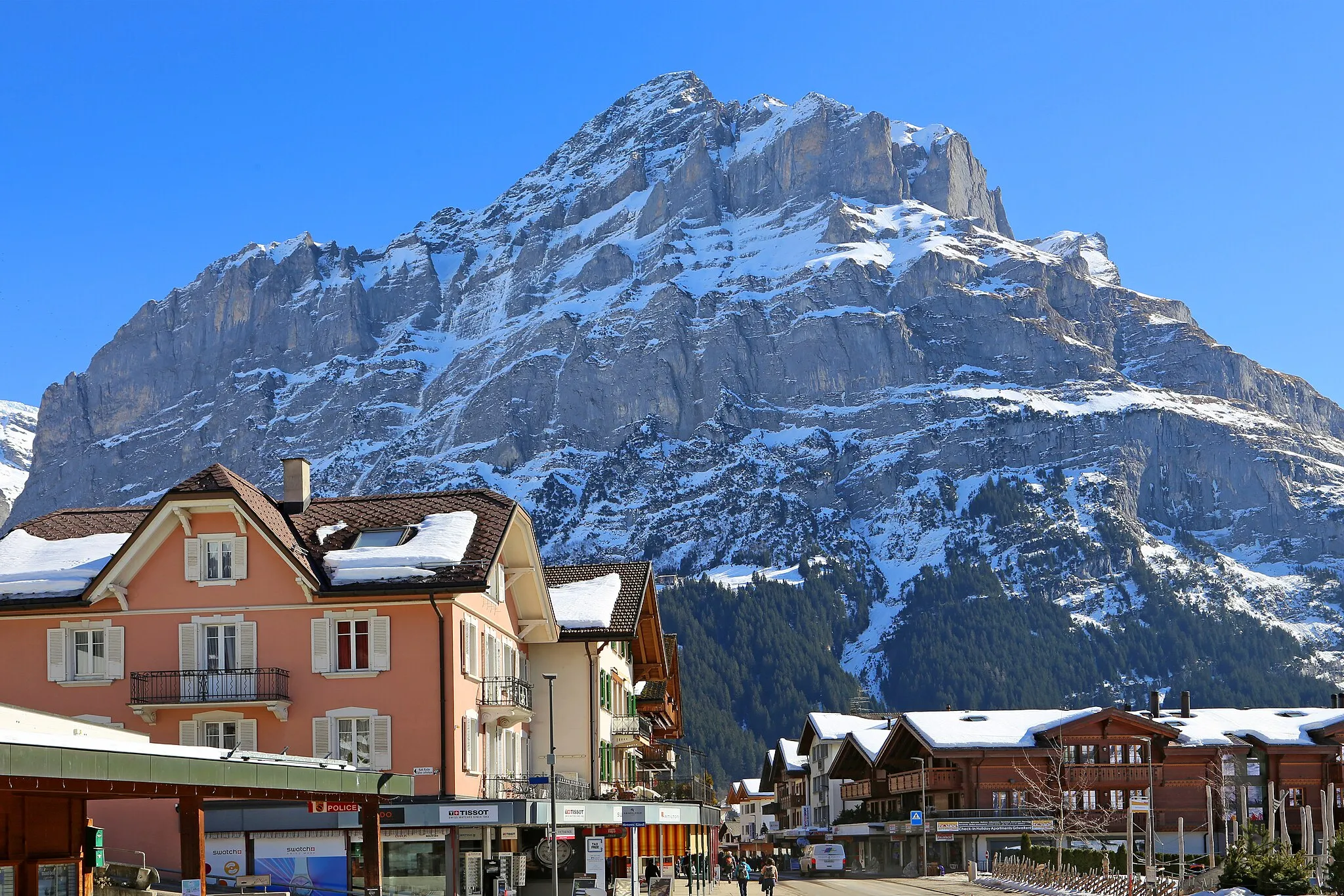 Photo showing: Grindelwald (view from Dorfstrasse 101) with Mettenberg. Grindelwald is a Swiss resort in the Bernese Alps (canton Bern). The Mettenberg above Grindelwald has an altitude of 3,104 meters above sea level. The station of Pfingstegg is visible near the centre of the image between the forests and the cliffs. NOT the Wetterhorn is the title suggests.