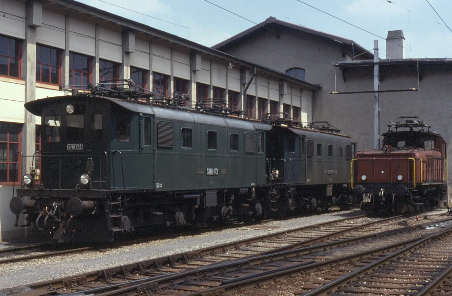 Photo showing: Seen stabled outside the depot at Huttwil on 8 July 1993 is a collection of locos owned (at the time) by three private operators albeit under one management. From left to right:
Solothurn-Münster-Bahn (SMB) Be 4/4 no. 172
Emmental-Burgdorf-Thun-Bahn (EBT) Be 4/4 no. 108
Vereinigte Huttwil Bahnen (VHB) Ee 3/3 no. 151 (ex SBB 16323)

These three standard gauge railways became known as the Regionalverkehr Mittelland (RM) and later swallowed up in to the BLS group of companies.