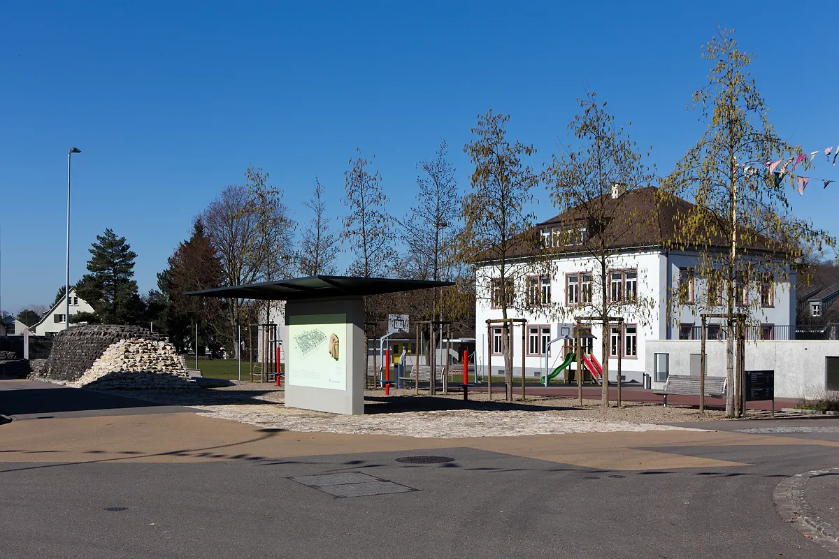 Photo showing: Dorfzentrum von Kaiseraugst (AG) mit römischer Kastellmauer, Info-Tafel zum Kastell, Dorfschulhaus und Parkhaus