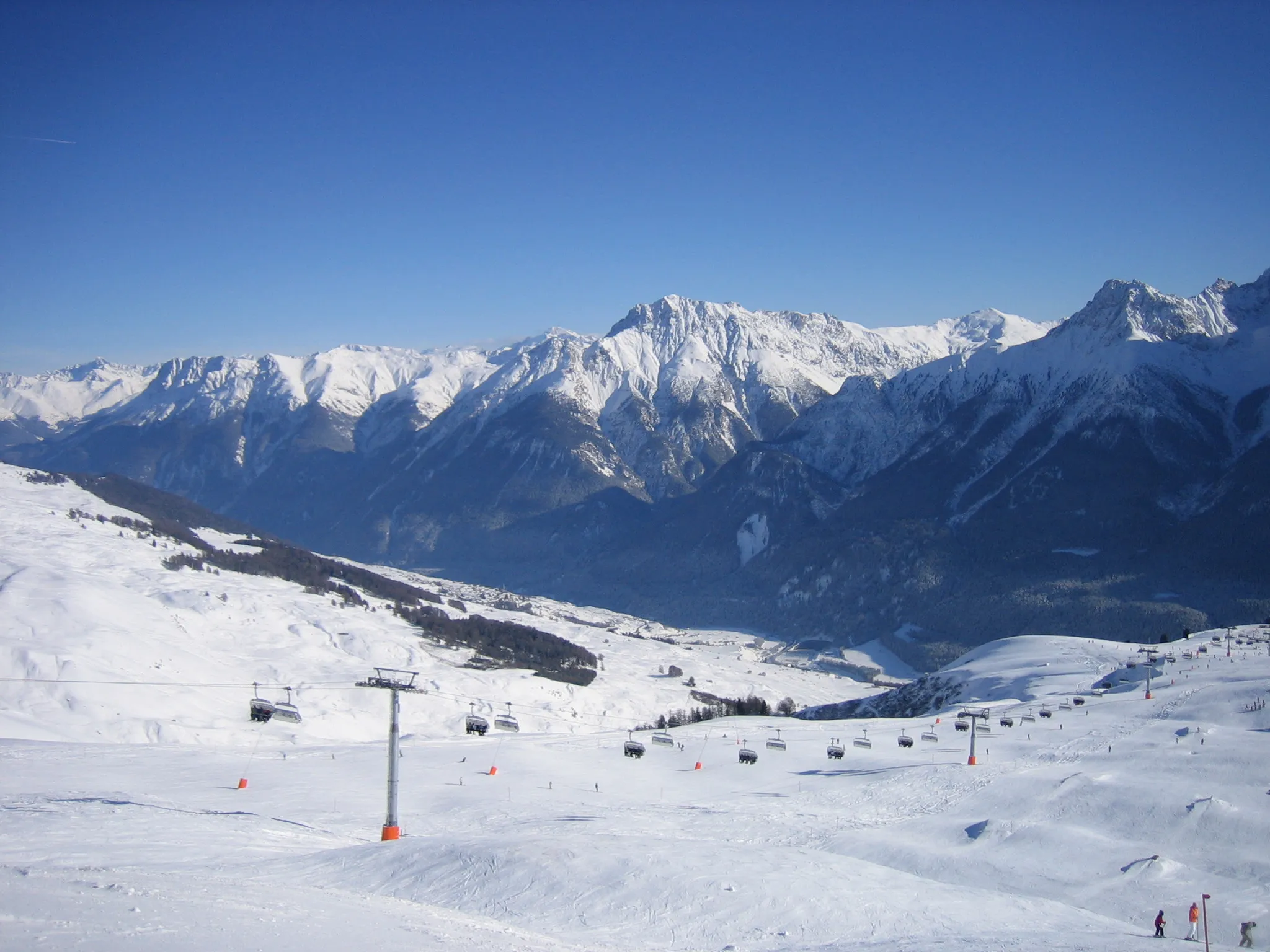 Photo showing: Blick von Schlivera (2300 m) über 6-er-Sessel Naluns Richtung Clozza Schlucht / Salez ins Tal. Leicht links der Mitte kann man unterhalb der Wälder am Sonnehang auf der Südhang-Terrasse Sent (1430 m) erahnen. 
Scuol liegt nicht sichtbar rechts im Talboden.