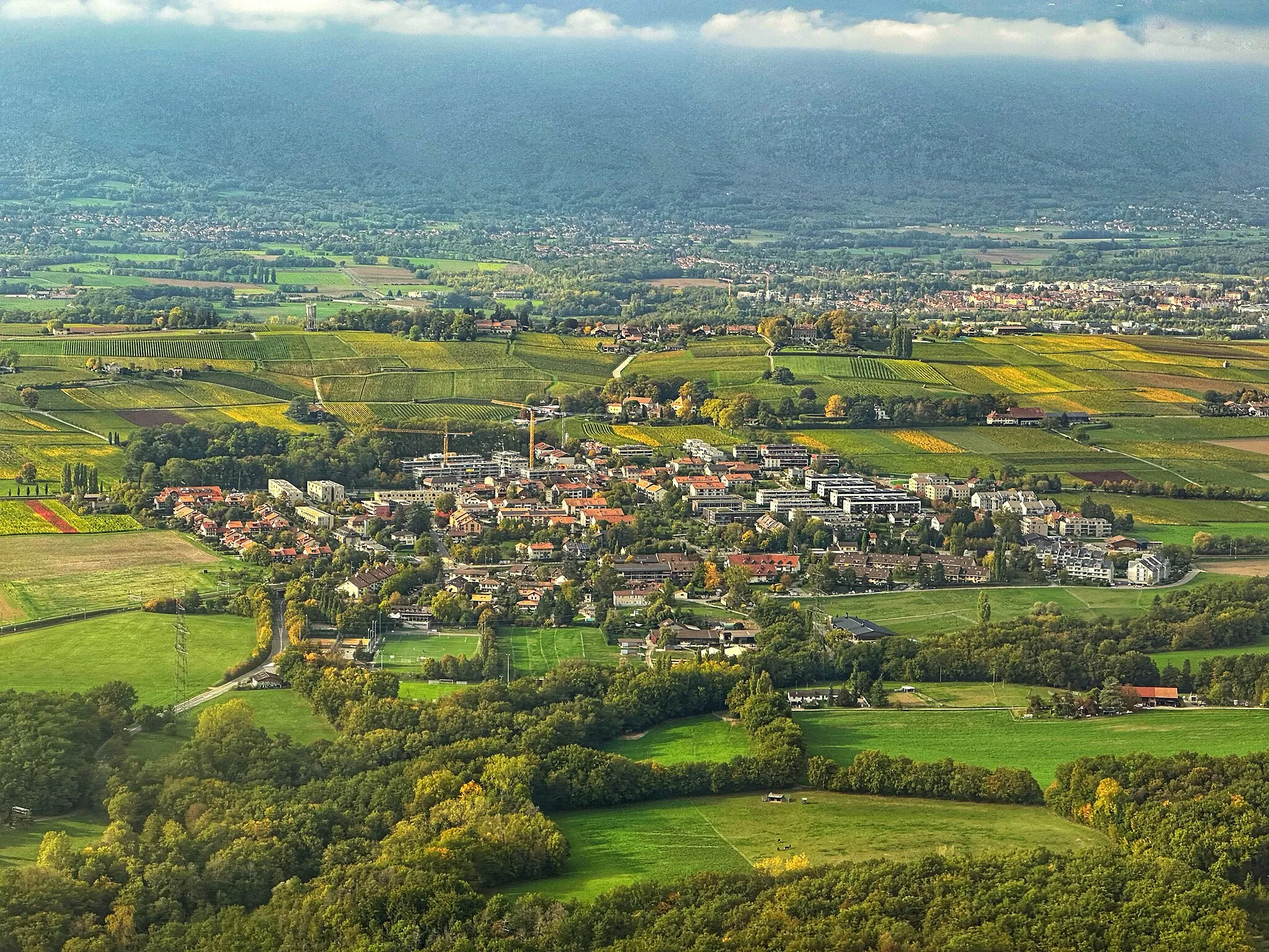 Photo showing: Vue du village principal de Satigny, avec le bois de Merdisel en premier plan et la chaîne du Jura en arrière-plan