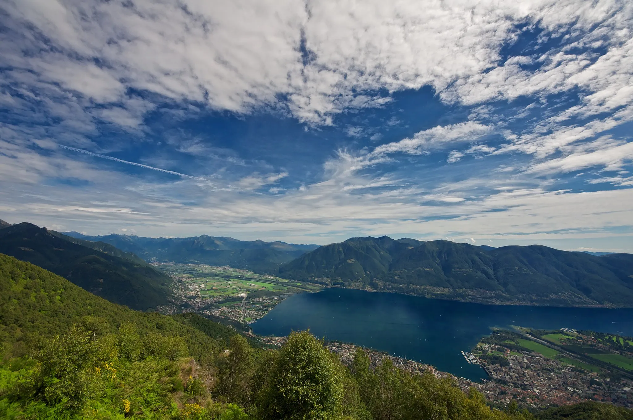 Photo showing: Looking South toward Lake Maggiore in Ticino, Switzerland. Locarno and Ascona are visible on the peninsula. Gambarogno is visible across the lake. Gordola is visible on the left at the end of the lake and Gudo is visible further up the valley.