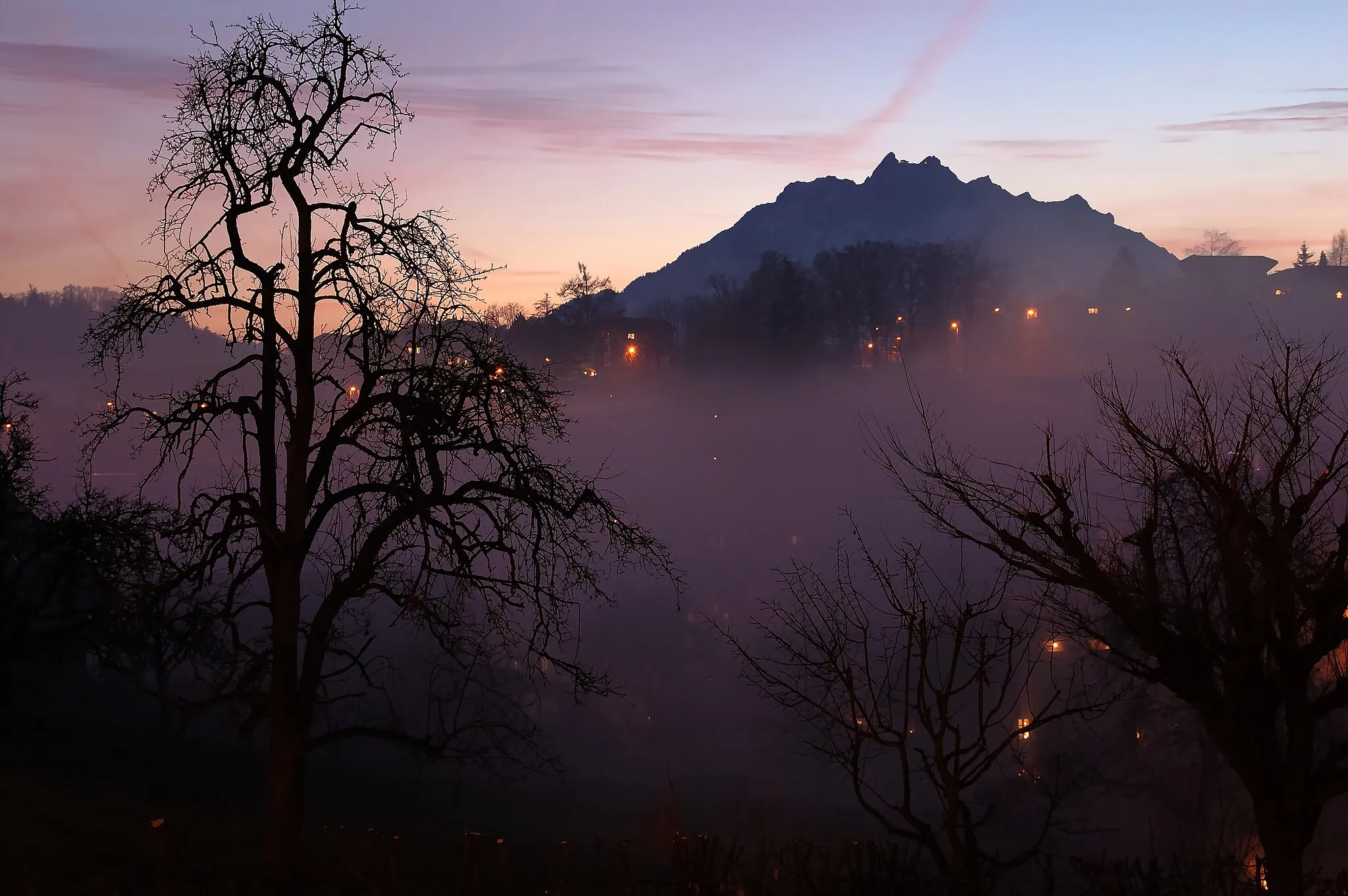 Photo showing: a foggy day ended in Adligenswil/Lucerne. But after sunset the fog disappeared slowly and mount Pilatus became visible. A great atmosphere