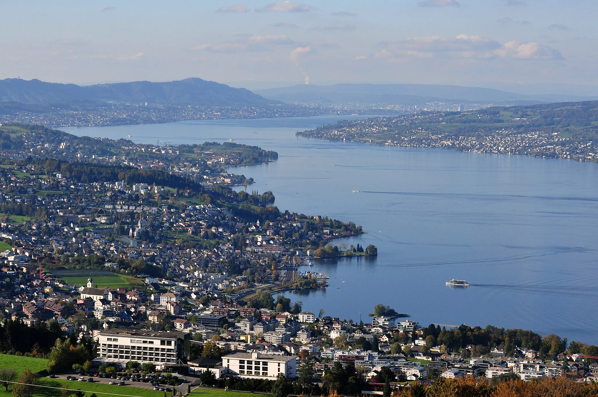 Photo showing: View from the Etzel mountain in Switzerland towards Etzel Kulm – focus on Richterswil : (from the left side) Richterswil and Horgen on Zürichsee lakeshore, Au peninsula, Albis chain with Felsenegg and Uetliberg, Zürich in the far background, Pfannenstiel (partially) to the right. Zürichsee-Schiffahrtsgesellschaft (ZSG) MS Säntis towards Rapperswil docking at Richterswil harbour, ZSG MS Panta Rhei is sailing towards Richterswil.