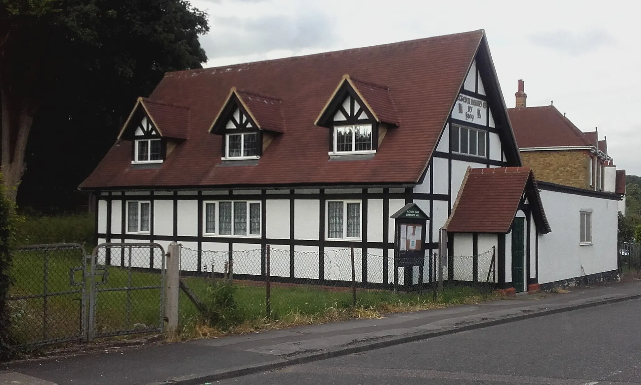 Photo showing: The Rucklers Lane Community Hall near Kings Langley, Hertfordshire. It was built for the workers of nearby Shendish Manor in 1909 as a memorial to Arthur Longman, the owner of the estate, and was originally intended as a chapel of ease to avoid the long walk to the parish church.