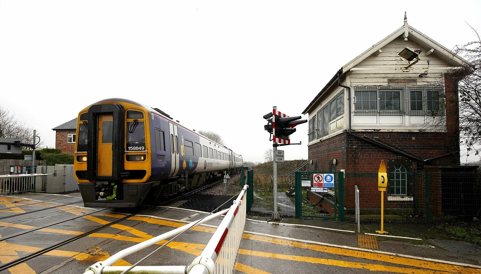 Photo showing: Common Lane in Brough leads to what the railway calls Welton Level Crossing, even though it is nowhere near the village of that name. Having lost the superb semaphore signs here 5 years ago, the box is still retained for crossing control on this busy section of main line.