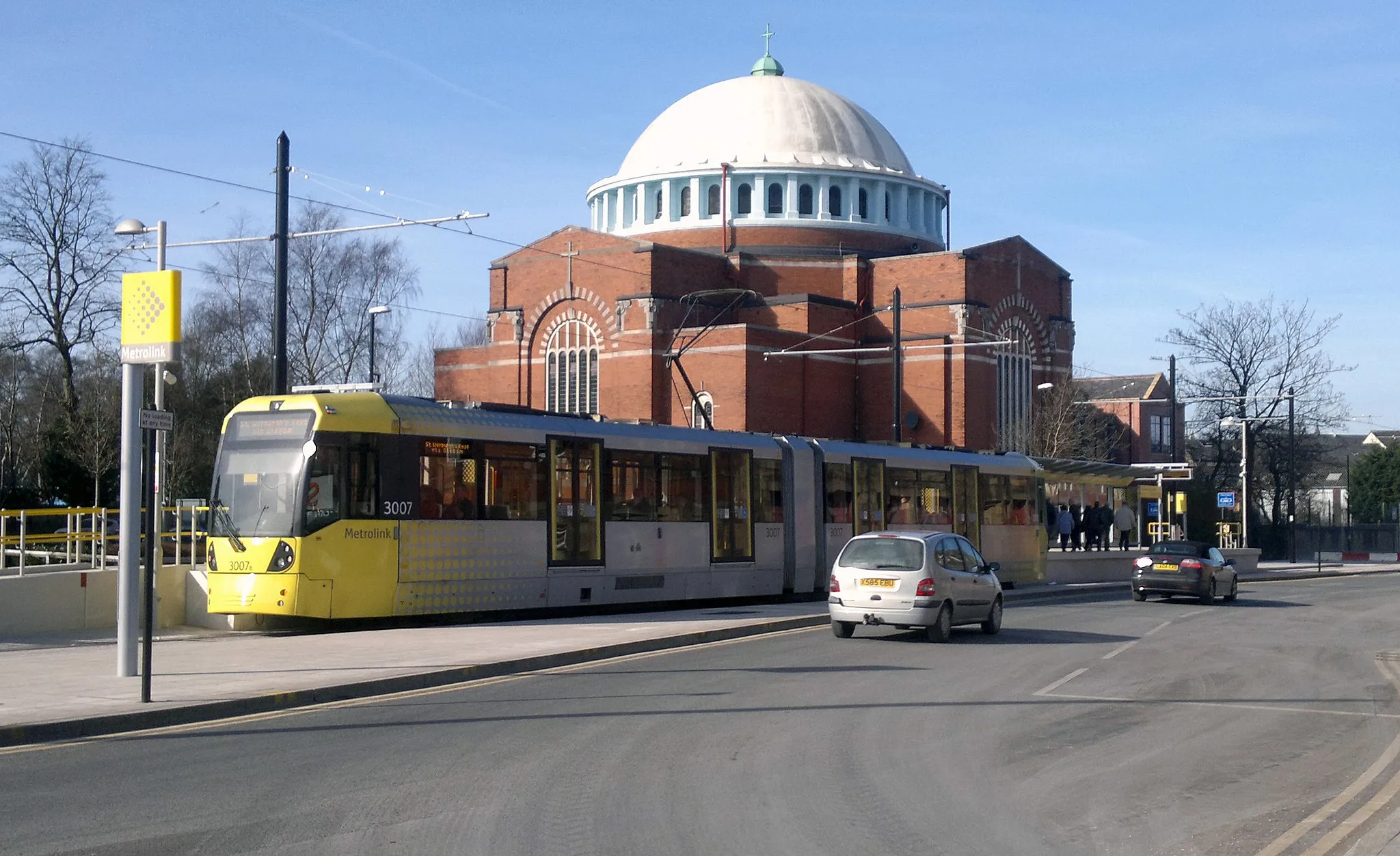 Photo showing: The Metrolink stop at Rochdale Railway Station, in Rochdale, Greater Manchester, England. This photograph was taken on the day Metrolink first started operating passenger services to Rochdale. Behind the stop is Rochdale's landmark St John the Baptist Catholic Church.