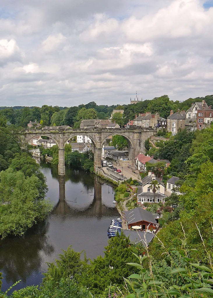 Photo showing: A famous view of the Knaresborough Viaduct across the River Nidd. The Church of St John the Baptist can be seen in the background, obscured by trees. This photo is taken from the hill after which the town is named, the site of the ruins of Knaresborough Castle (borough derives from an Old English word meaning ‘fortress’).