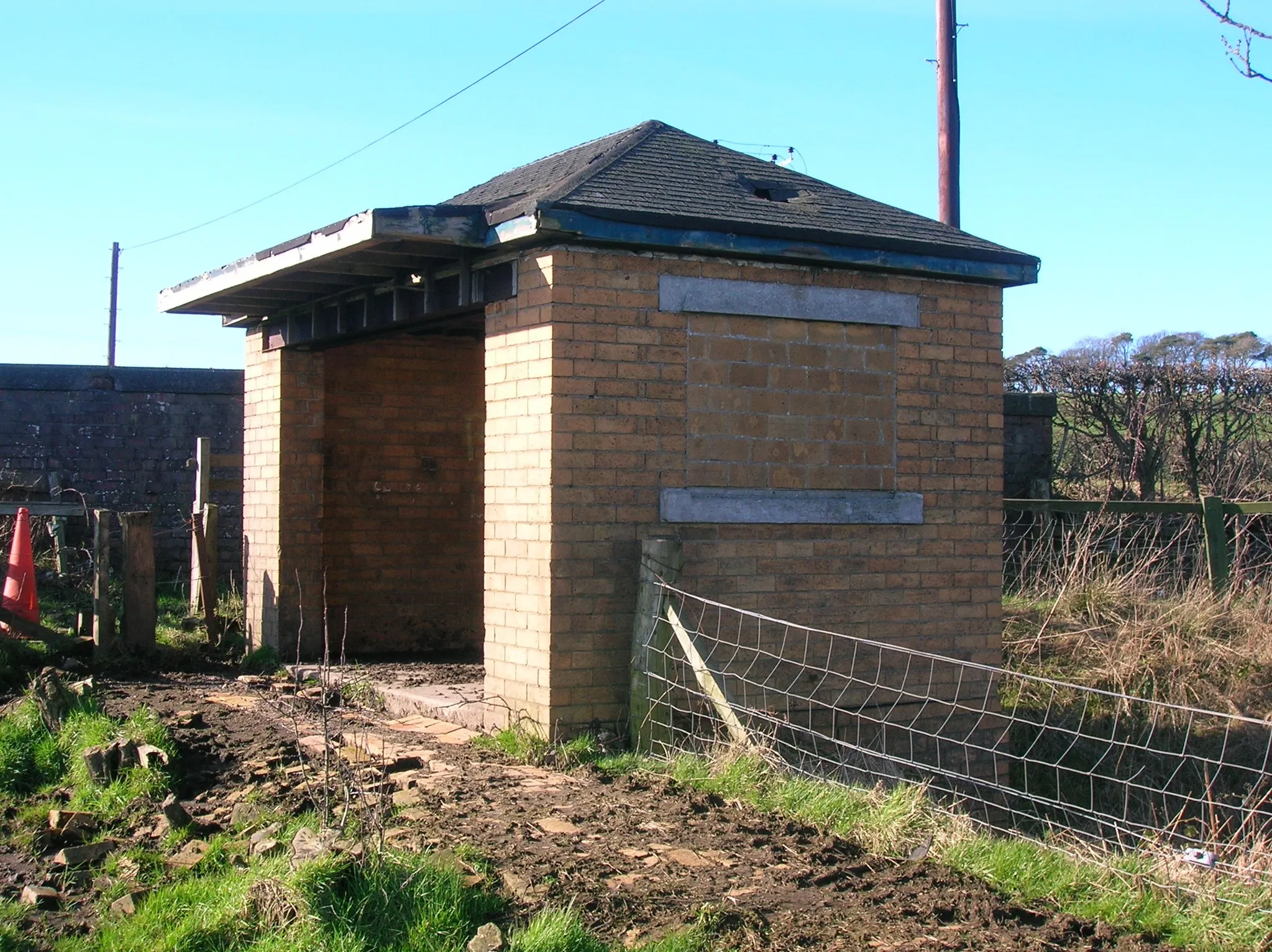 Photo showing: The controller cabin on the Monkcastle fireclay mine railway incline, Dalry, Ayrshire, Scotland. This was once a shelter for brick works employees who had to walk up the narrow-guage railway tracks to get to the main road where they could catch a bus. The current access road and bridge are more recent additions, as formerly vehicular access to the works was by a road which connected to the area near the railway station, almost a mile to the north. The building is open on the southerly side, and originally had windows on the others, which have been bricked in. There is no need for a control cabin, as the railway was a gravity system, with the small cars connected to a cable, which allowed the weight of the loaded cars to return the empty ones back up to the mine.