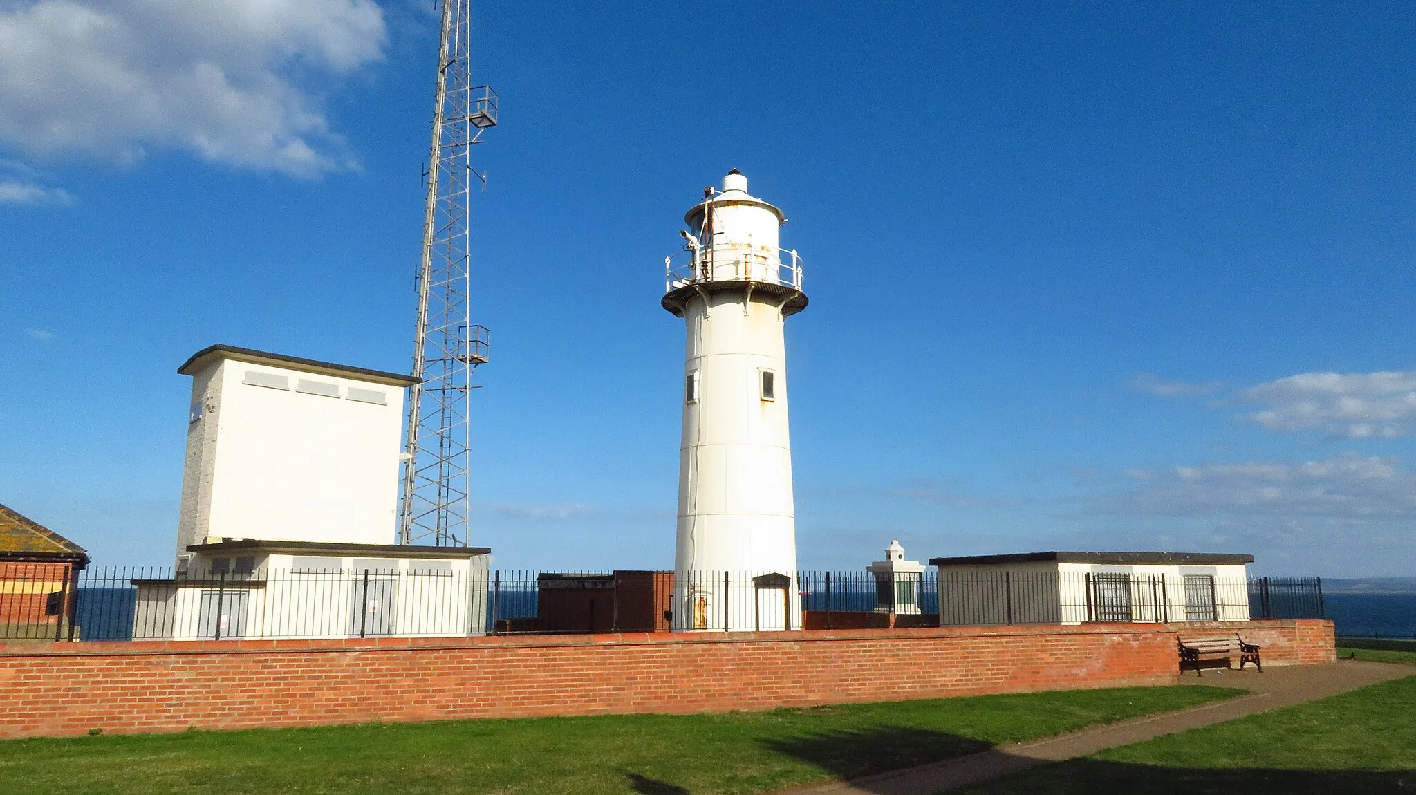 Photo showing: Established in 1847, the original Heugh Lighthouse was the first to be powered by natural gas produced from local coal mines. It displayed a subsidiary red light lower down the tower depending on the state of the tide. It was demolished in 1915 as it obstructed the line of fire from the headland battery. A temporary wooden lattice tower was erected on the Town Moor and the lantern and lens from the lighthouse were relocated to the new tower. The current lighthouse replaced the lattice tower in 1927 and is 13 metres high.