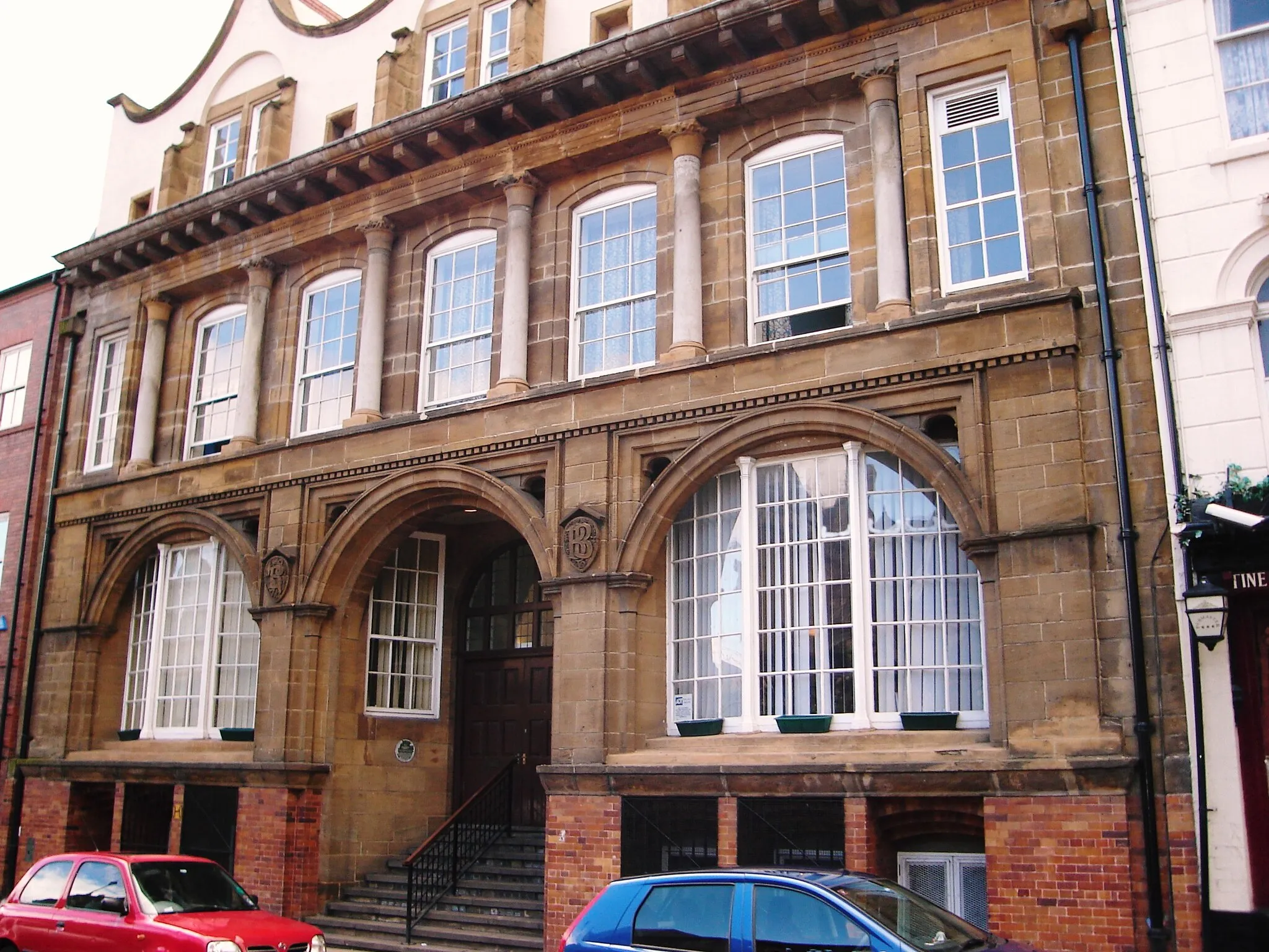 Photo showing: Former Bell Brothers Offices
Zetland Road, Middlesbrough. Designed by Philip Webb his only remaining commercial building. 
Now called Webb House.
This photograph was linked in the article in the Guardian "The Northerner" Blog - 17th October 2011
[www.guardian.co.uk/uk/the-northerner/2011/oct/17/middlesb...]
English Heritage
"MIDDLESBROUGH ZETLAND ROAD, NZ 4920 NE south side.
8/97 No. 7 (Formerly listed as offices 13.2.63 occupied by Dorman Long & Co. Ltd.). G.V. II* Offices, 1881/91 by Philip Webb, for Hugh Bell, ironmaster. Altered and extended 1906 by George Jack. Sandstone ashlar; glazed brown brick basement; rendered brick attic storey, with stone dressings; renewed rendered brick stacks; renewed render at rear and renewed clay pantile roof. Arts and Crafts classical style. 2 storeys, with basement and attic storey. 3-bay ground floor and attic, 7-bay first floor and basement. 9 steps up to central renewed double doors, under mullioned-and-transomed fanlight. Flanking renewed sash windows in splayed reveals, deeply recessed behind round-headed opening and segmental archivolt springing from moulded corbels on slender hexagonal pilasters with trumpet capitals. Narrow impost strings; and spandrels with shields enriched with raised lettering : "B. 1891" and "B.B". Recessed canted windows, with 18-pane fixed lights and similar pilasters at angles, in similar segment-headed openings. Stepped sills. Dentilled band between floors. Renewed 15-pane sash windows, in middle 5 bays on first floor, recessed behind colonnade with moulded bases and waterleaf capitals, under continuous frieze and-projecting bracketed cornice. 10-pane fixed-light windows in end bays. Renewed basement windows, deeply recessed in stepped segment-vaulted surrounds with iron grilles, flank the entrance steps. Concave gables, with moulded copings, over each bay of attic storey. 2-light mullioned 8-pane sash windows, recessed in round-headed openings with blind tympana; each window flanked by buttresses with scrolled ramped tops. Rainwater openings with flat surrounds, between bays and at ends. End and ridge stacks. 8-bay rear has renewed segment-headed 15-pane sash windows, recessed in round-headed arcade on ground floor. Altered windows in 5 left bays. Blind right end bay. Similar sash windows on first floor, the 5th bay blind, under projecting segmental arcade on corbel imposts. Dentilled sill band. Renewed sashes in attic storey, the 4th bay blank; blocked oculus in right end bay. 9 segment-headed basement windows with iron grilles, 2 at left end boarded up. 6-panel door under blind segmental head at right end. Interior altered. Webb's only office building; drawings in R.I.B.A. Library. Being converted to flats and workshops at time of resurvey.
Listing NGR: NZ4954520634
Selected Sources
Legacy Record - This information may be included in the List Entry Details

National Grid Reference: NZ 49545 20634"