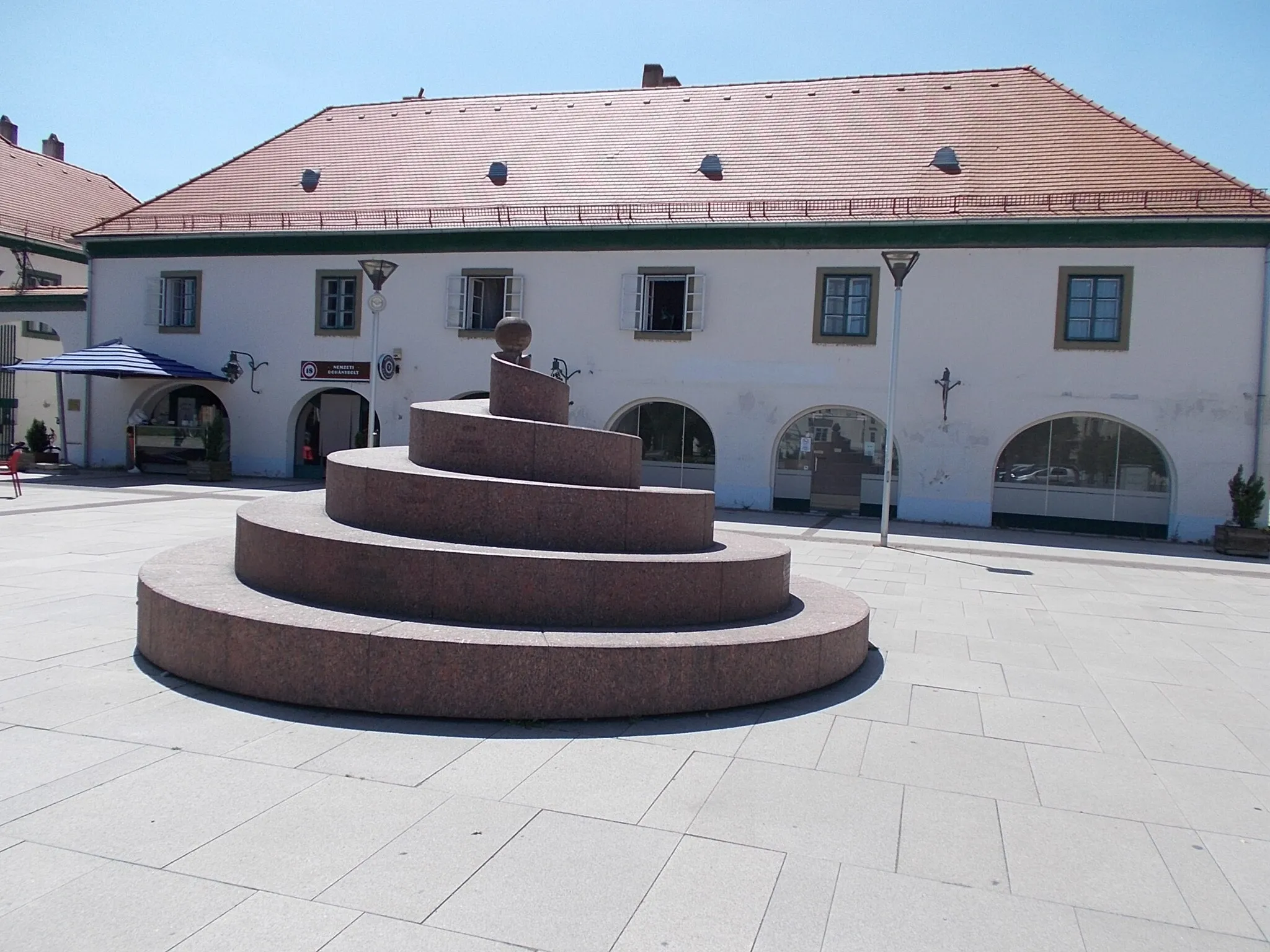 Photo showing: Spiral fountain /other titles: "Time spiral" 'Körmend history memorial' /  Planned by architect Miklós Sólyom. Installed in 2010 (2012?)  The water bubbling out of the turned spring stone placed at a height of 2.25 meters flows down the spiral surface, 53 meters long, on a very low slope of 2-3%. The sculpture is a spectacle, a water playground and a memorial site for important dates of the city.' - Szabadság Square, Körmend, Vas County, Hungary.