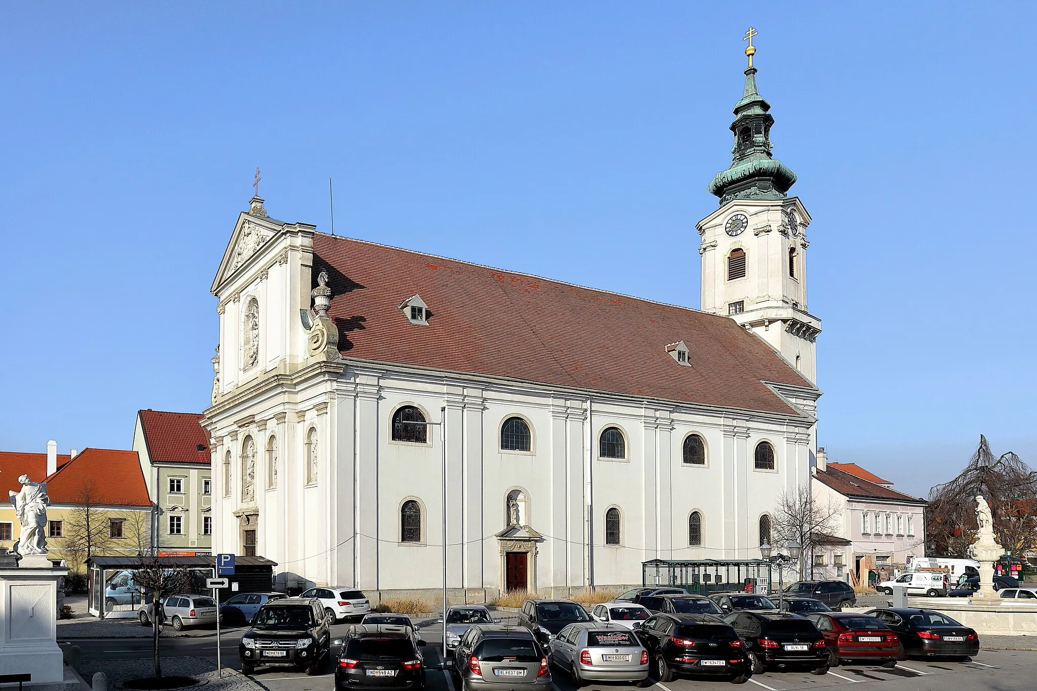 Photo showing: Südostansicht der röm.-kath. Pfarrkirche hl. Dreifaltigkeit in der niederösterreichischen Stadtgemeinde Bruck an der Leitha. Links der Sockel mit einer Statue der 1707 errichteten Mariensäule und rechts der 1713 erbaute Florianibrunnen. Die Kirche wurde von 1696 bis 1702 unter Einbeziehung des Stadtturmes errichtet. Dieser ist bis zum Schallgeschoss mittelalterlich (um 1230). Der Umlaufgang wurde im 16. Jahrhundert errichtet und das barocke Glockengeschoss um 1740. Die schmucklose Stirnfront wurde ebenfalls in dieser Zeit (1738–40) umgebaut. Unter anderem wurde sie mit einem geschosstrennenden Gebälk, einem giebelbekrönten Obergeschoss und einem dreiachsigen Mittelrisalit gegliedert. Zusätzlich wurden 6 Rundbogennischen für Steinstatuen eingebaut.