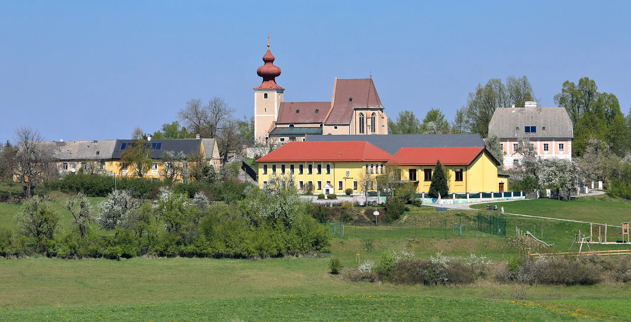 Photo showing: Südansicht des Kirchenweilers Sankt Johann in Großheinrichschlag, ein Ortsteil der niederösterreichischen Gemeinde Weinzierl am Walde. Die weithin sichtbare röm.-kath. Pfarrkirche von Großheinrichschlag ist dem hl. Johannes der Täufer geweiht. Der mächtige mittelalterliche Turm mit wuchtigem, barockem Zwiebelhelm ist der Westfront vorgestellt und der stark überhöhte Chor im Osten wurde in der 2. Hälfte des 15. Jahrhunderts errichtet.