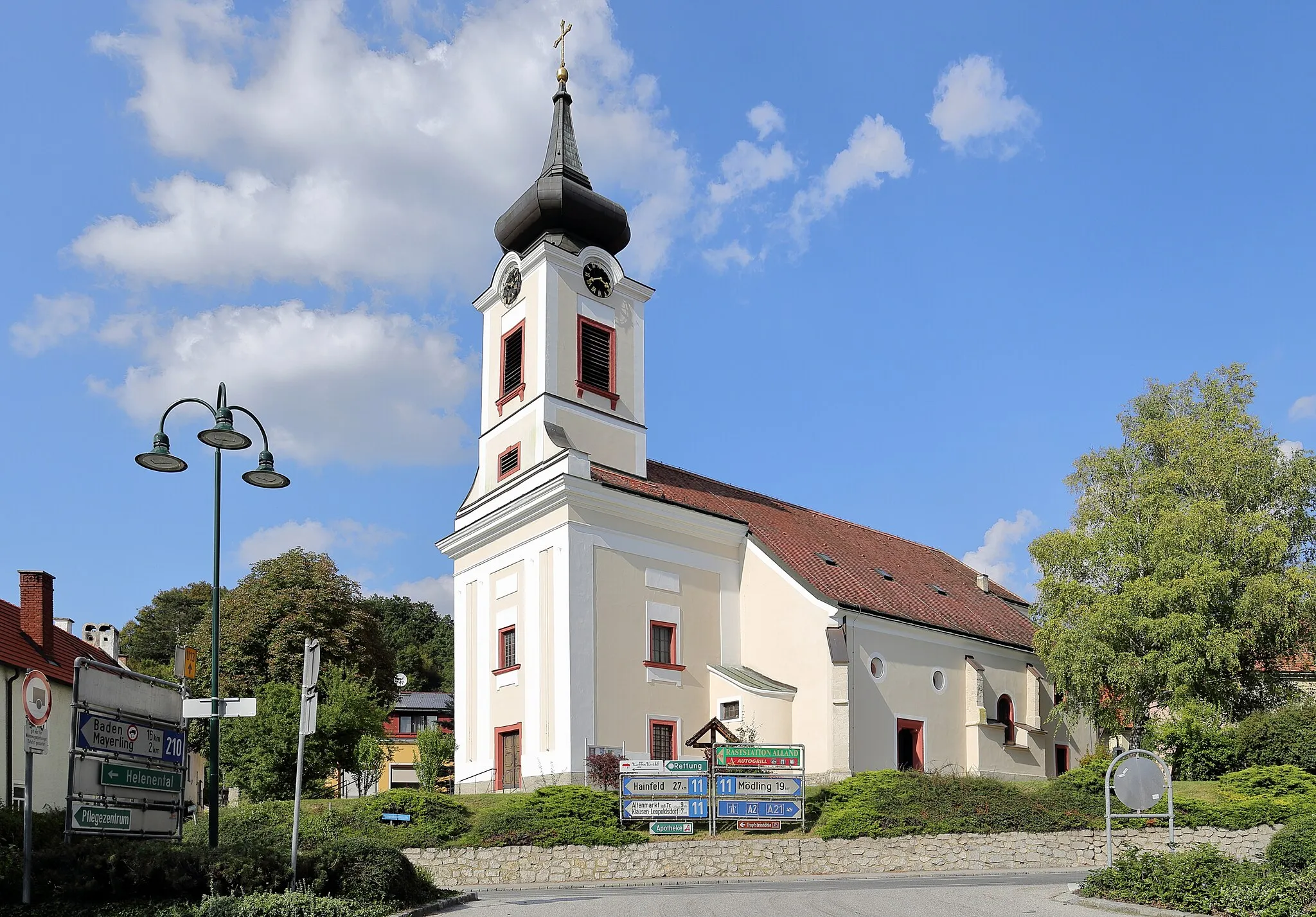 Photo showing: Südansicht der röm.-kath. Pfarrkirche hll. Georg und Margarethe der niederösterreichischen Gemeinde Alland. Ursprünglich eine romanische Saalkirche. Im 12. Jahrhundert wurde diese um ein Nordschiff und einen Westturm erweitert. Im 14. Jahrhundert erfolgte der Anbau einer Südostkapelle, die Einwölbung des Nordschiffes sowie der Neubau des Chores. Um 1500 Zubau eines 2. südlichen Seitenschiffjoches und des Südportales. Um 1800 Neubau der oberen Geschosse des Turmes und Barockisierung der Fassade. Im Zuge der Kriegshandlungen 1945 stürzte das zweijochige Mittelschiff und das Südschiff ein und wurde bis 1954 wiederaufgebaut. Bei den zwei Türkenbelagerungen (1529 und 1683) wurde die Kirche ebenfalls schwer beschädigt und jeweils wiederinstandgesetzt.