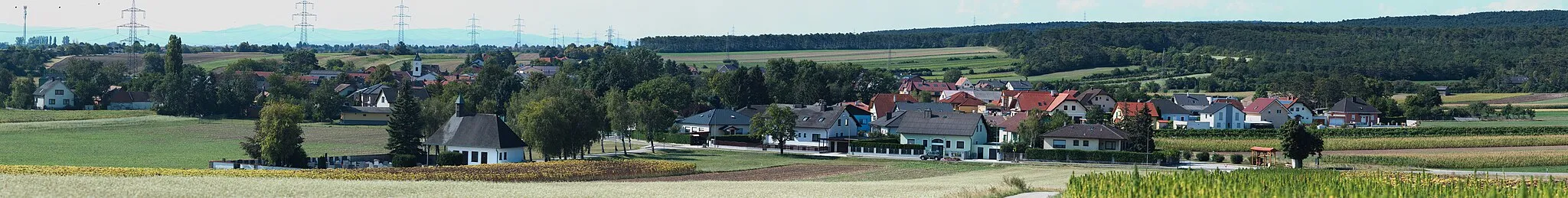 Photo showing: Panorama des Ortsteiles Hölles der Gemeinde Matzendorf-Hölles, Bezirk Wiener Neustadt, Niederösterreich, Österreich.
Zu sehen sind im Vordergrund der Gemeindefriedhof, im Mittelgrund die Ortskapelle des Hl. Kolomann und im Hintergund die Ortskirche von Steinabrückl. In der Bildtiefe sind die Bucklige Welt und das Rosaliengebirge gerade noch auszumachen.

Das Panorama setzt sich aus 115 Einzelaufnahmen zusammen. Objektiv: Canon 70-300mm 1:4-5.6 IS USM