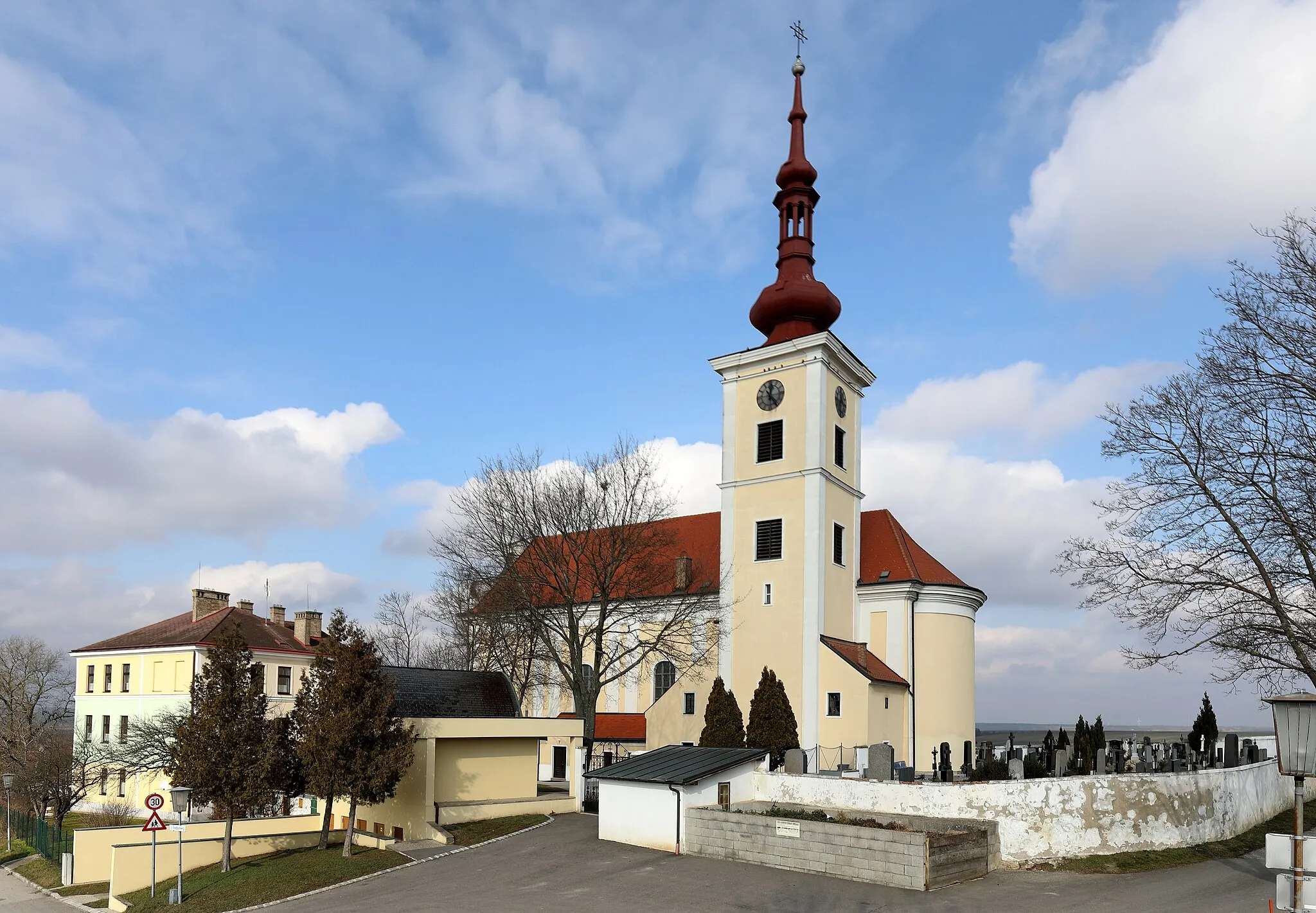 Photo showing: Südansicht der katholischen Pfarrkirche Hl. Kreuz in der niederösterreichischen Marktgemeinde Hohenruppersdorf mit Friedhof und links dem Gebäude der neuen Mittelschule. Die Kirche ist ein in erhöhter Lage von 1788 bis 1790 errichteter barocker Sakralbau mit einem mächtigen Südturm, der im Kern mittelalterlich ist.