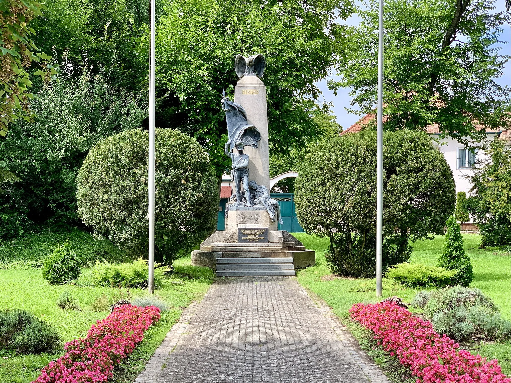 Photo showing: Das Kriegerdenkmal wurde auf Initiative des Postmeisters Anton Pfalz geplant, finanziert und am 4. Juli 1909 anlässlich der Gedenkfeier "100 Jahre Schlacht bei Wagram" unter Bürgermeister Ferdinand Leeb enthüllt. Es stammt vom Wiener Bildhauer Franz Seifert (1866-1951), der als Gutsverwaltersohn in Schönkirchen geboren wurde. Das Denkmal stellt einen österreichischen Grenadier des 42. Infanterie-Regiment mit hochgehaltener Fahne dar. Das Regiment zeichnete sich bei den Marchfeldschlachten besonders aus und erhielt von Erzherzog Carl dafür die Genehmigung „allzeit den Grenadiermarsch schlagen zu dürfen“. Die Tradition dieses Regiments wird im Heimat- und Napoleonmuseum Deutsch-Wagram dargestellt. Auf der gegenüberliegenden Straßenseite erinnert eine Gedenktafel an einen Irrtum des sächsischen Korps am 5. Juli 1809 abends. Dieser führte zu hohen Verlusten bei den angrreifenden Sachsen ("Sachsenklemme")