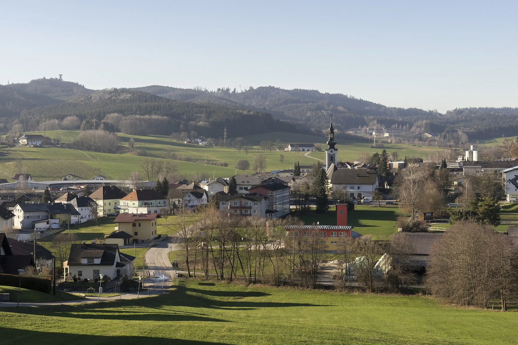 Photo showing: Ampflwang, Gesamtansicht. Links oben der Aussichtsturm Göblberg. Darunter die Remise des Lokparks. Rechts die Kirche, die Feuerwehr und das Reitzentrum. Im Hintergrund der Robinson Club.