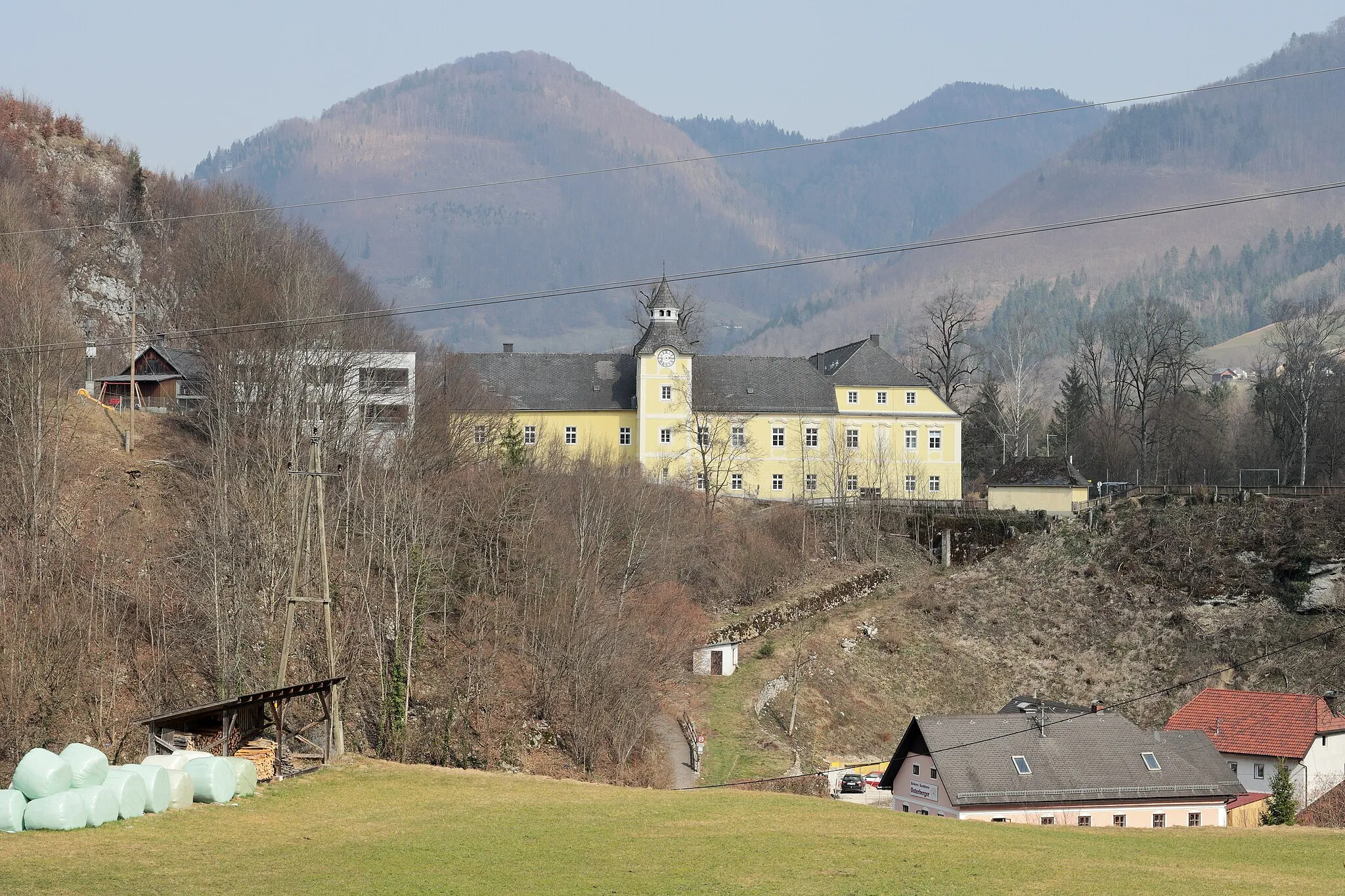 Photo showing: Grünburg: Blick vom Osterbergerberg über den Graben des Schmiedleitnerbaches (Rinnerbach) auf Schloss Leonstein. Unterhalb des Schlosses befinden sich Reste der alten Steyrtalstraße. Die Häuser im Talgrund sind Priethal 3 (Bäckerei Osterberger) und Priethal 4.