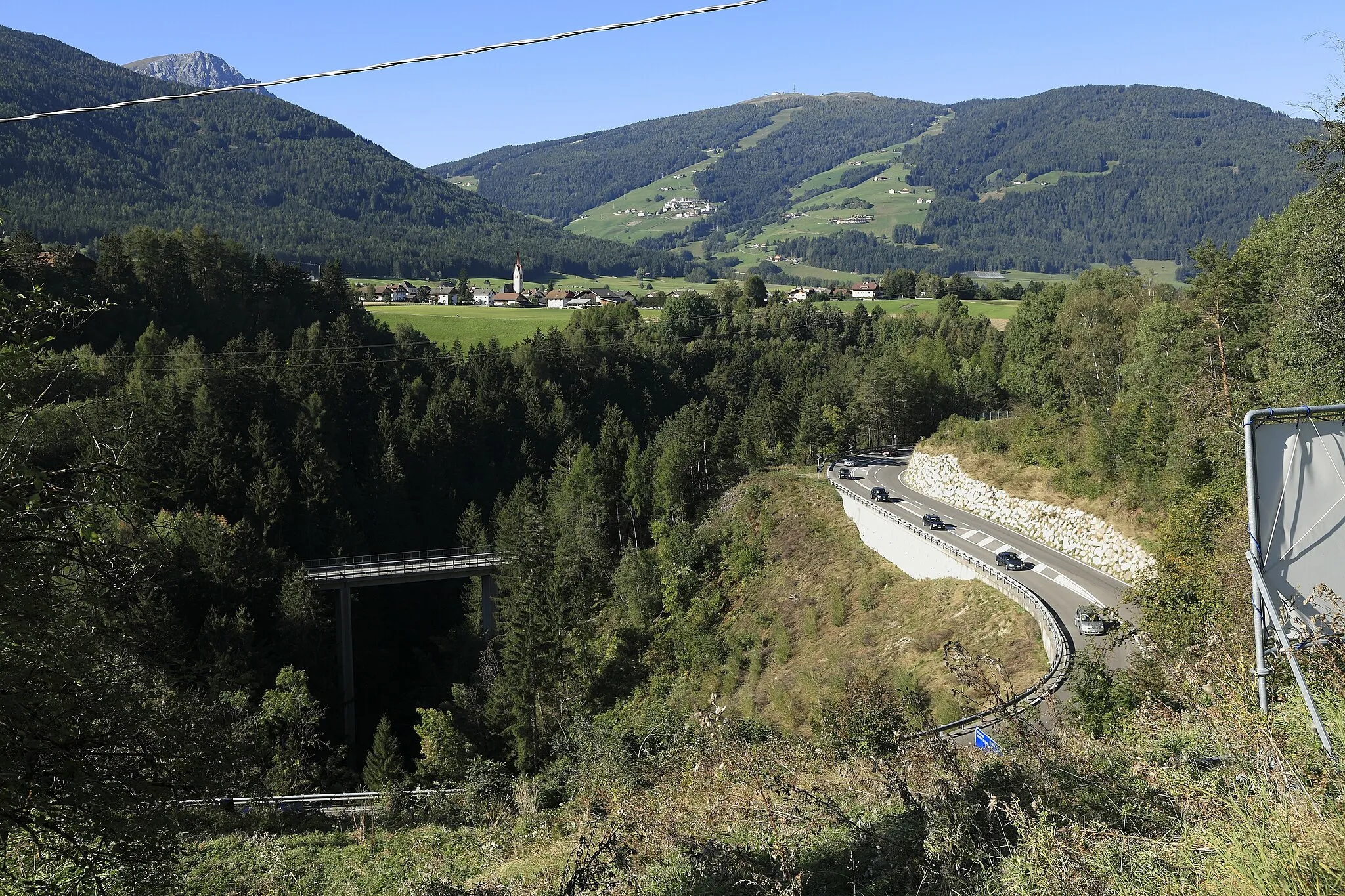 Photo showing: Von der Göste oberhalb der Staumauer des Olanger Stausees Richtung Westsüdwest, die Staatsstraße 49 verläuft rechts im Anschnitt durch den Hang. Links im Talgrund liegt Oberolang mit der Kirche Maria Himmelfahrt, rechts darüber am Hang Geiselsberg.