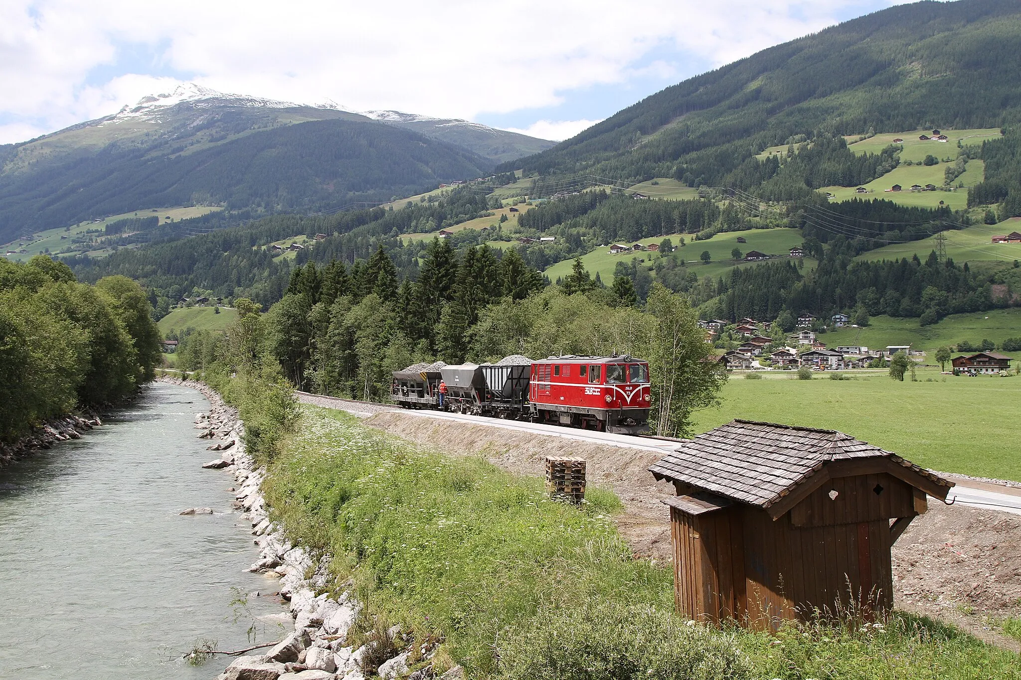 Photo showing: A ballast train passing Sulzbachtäler halt. The station shelter is awaiting to be placed on the platform. View heading NW, Neunkirchen-Venedigersiedlung, above Gernkogel and Laubkogel (2317 m), in clouds.