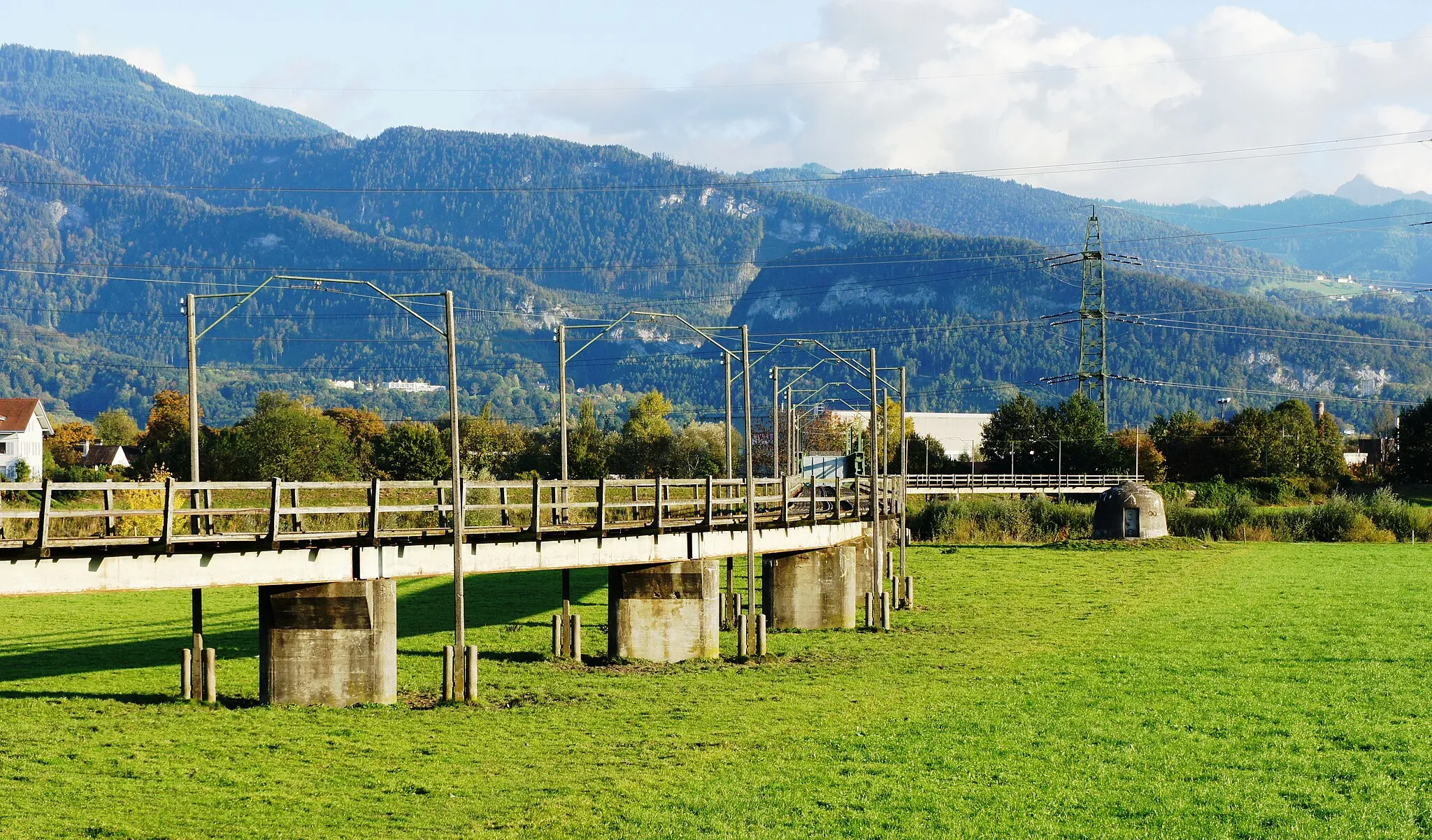 Photo showing: Nahaufnahme aus Nordwesten der Brücke der Dienstbahn der Internationalen Rheinregulierung bei Kriessern. Hinter den Bäumen auf der anderen Seite des Rheins liegt Mäder (A). Im Hintergrund Berge im Vorarlberg.