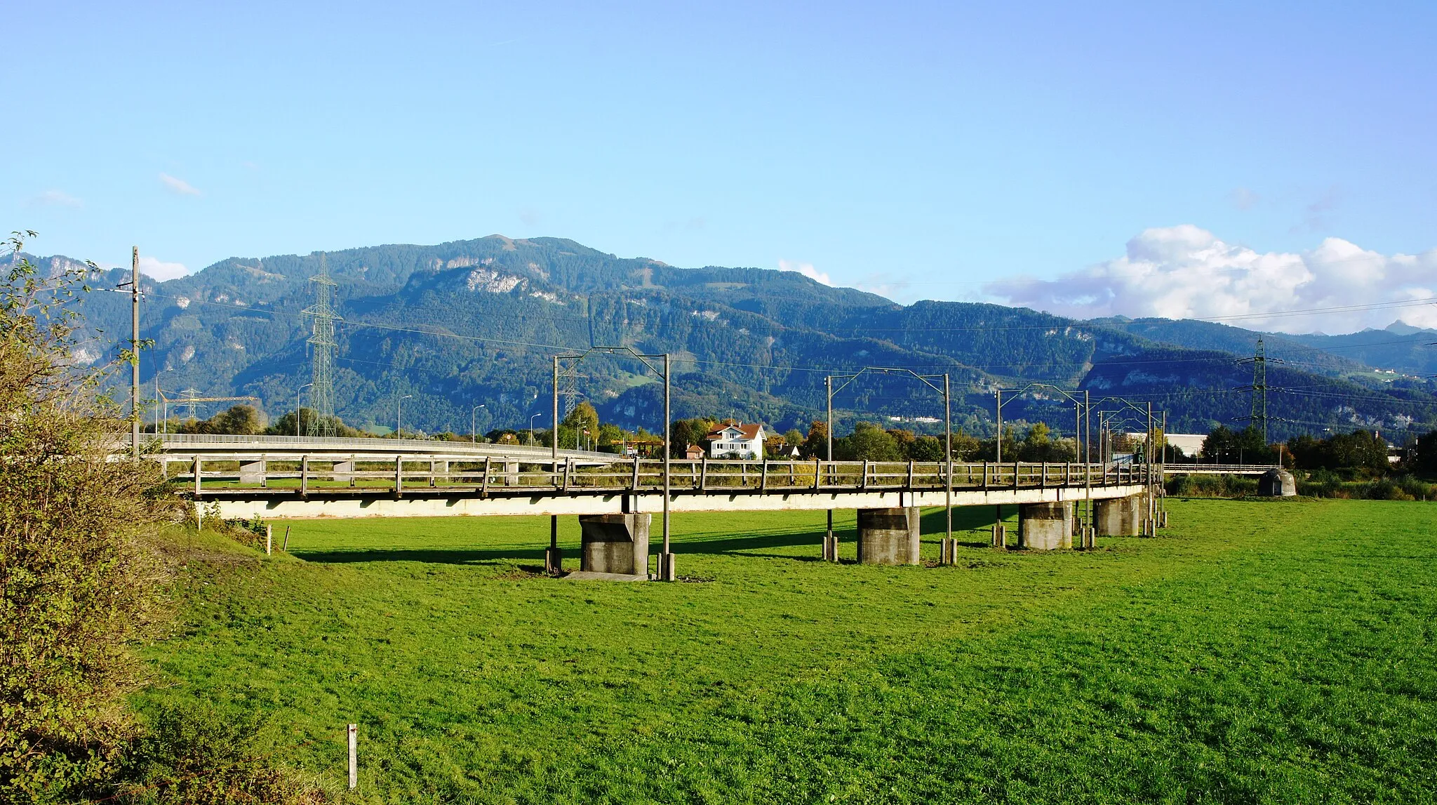 Photo showing: Blick aus Nordwesten auf die beiden Brücken über den Rhein von Kriessern nach Mäder. Im Vordergrund die Brücke der Dienstbahn der Internationalen Rheinregulierung, links dahinter die Strassenbrücke. Im Vordergrund das Rheinvorland (Hochwasserschutz) und im Hintergrund Berge im Vorarlberg.