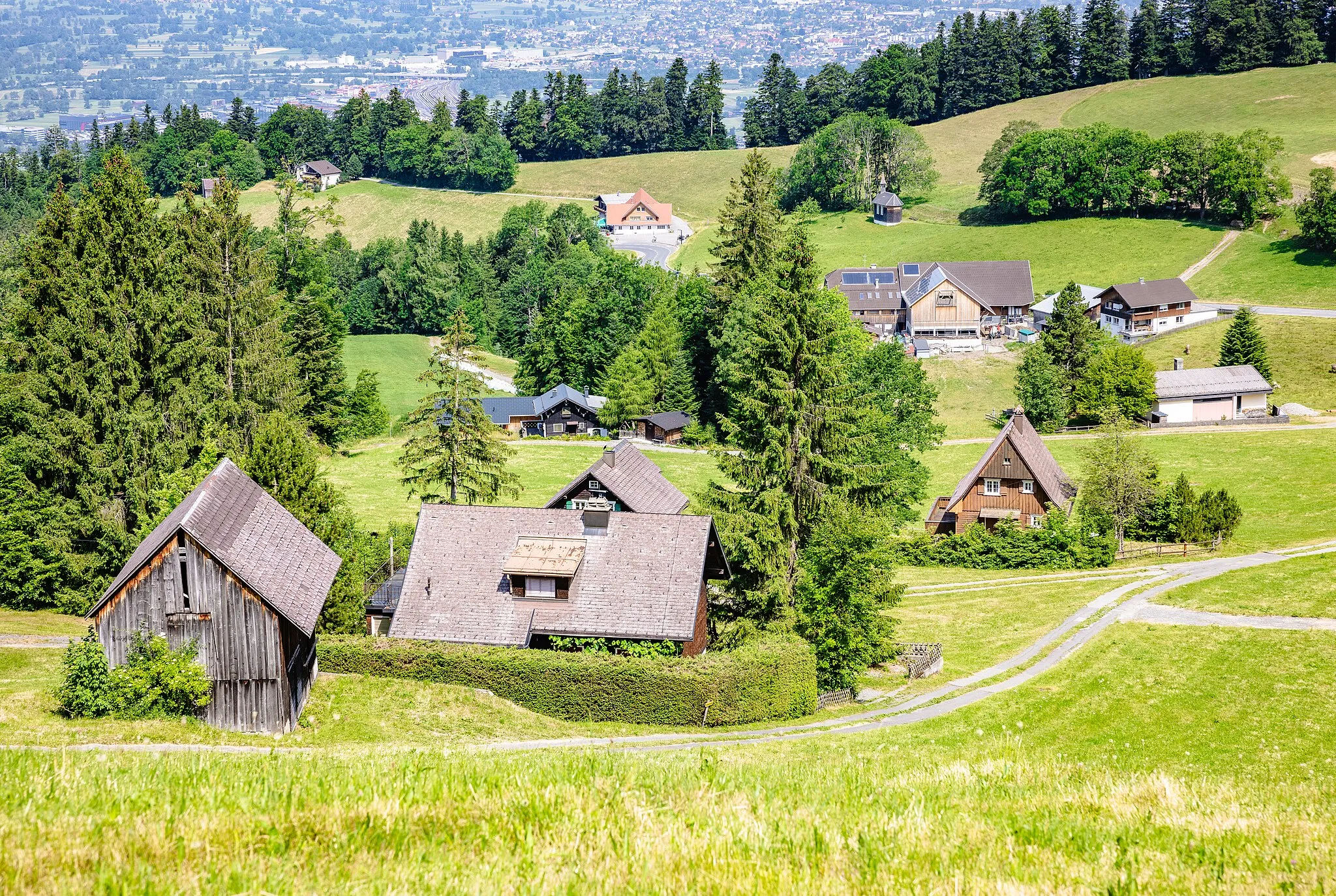 Photo showing: Ammenegg ist ein Ortsteil von Dornbirn auf halbem Weg zwischen dem Stadtkern und dem Bödele. Auf dem Foto blickt man in Richtung Nord-West auf die Streusiedlung und das Rheintal. Im Hintergrund mittig sieht man an der Bödelestraße das Gasthaus "Ammenegger Stuba" und rechts davon die Kapelle.