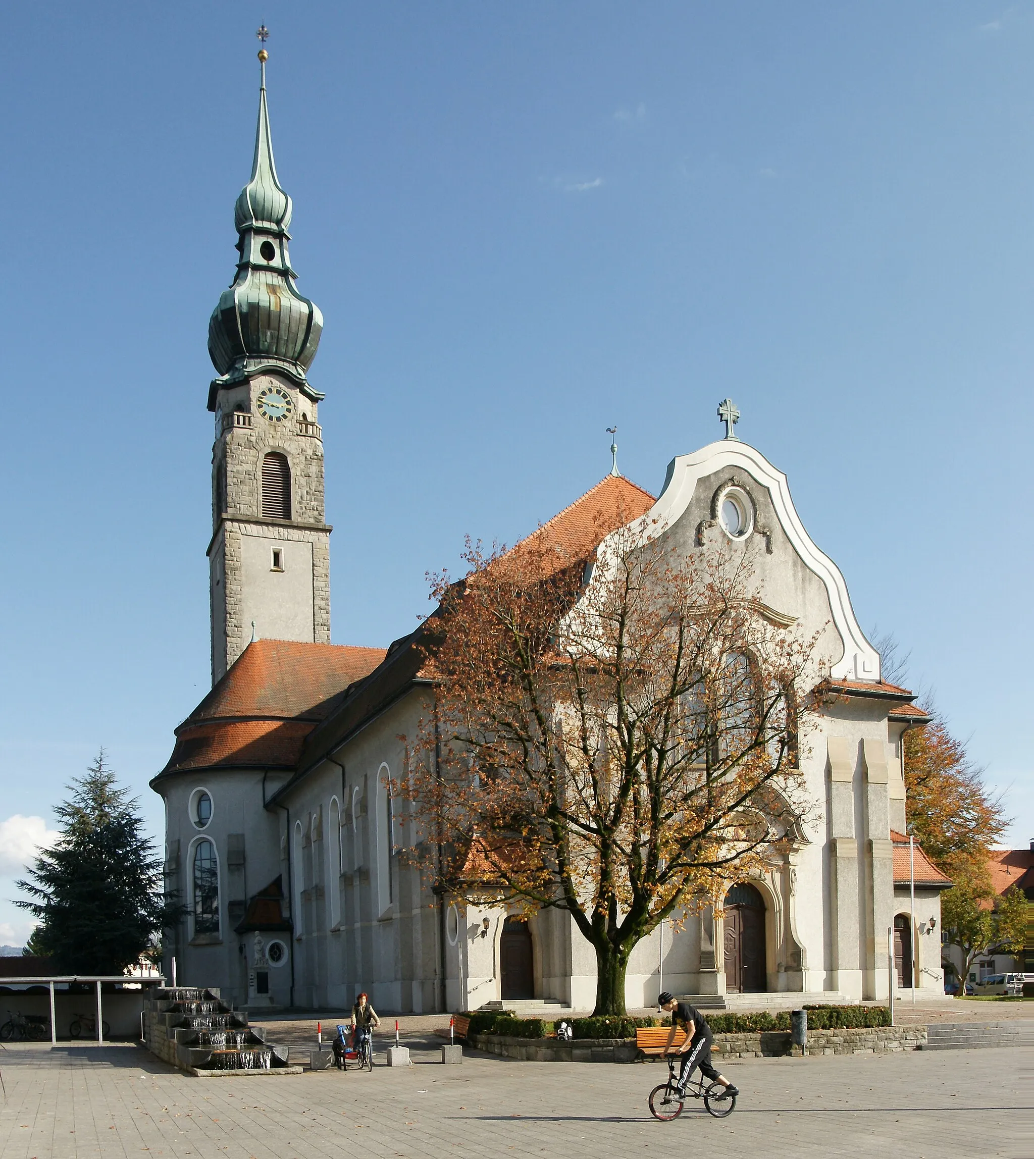 Photo showing: Pfarrkirche hl. Johannes dem Täufer., in Höchst (Vorarlberg). Im Norden Friedhof mit Arkaden. Mächtige neobarocke Kirche mit Querschiff, geschwungener Giebelfassade und schlankem Nord-Turm mit Zwiebelhaube. Heutiger Bau 1908-1910 nach Plan von Albert Rimli durch Baumeister Cornel Rhomberg.