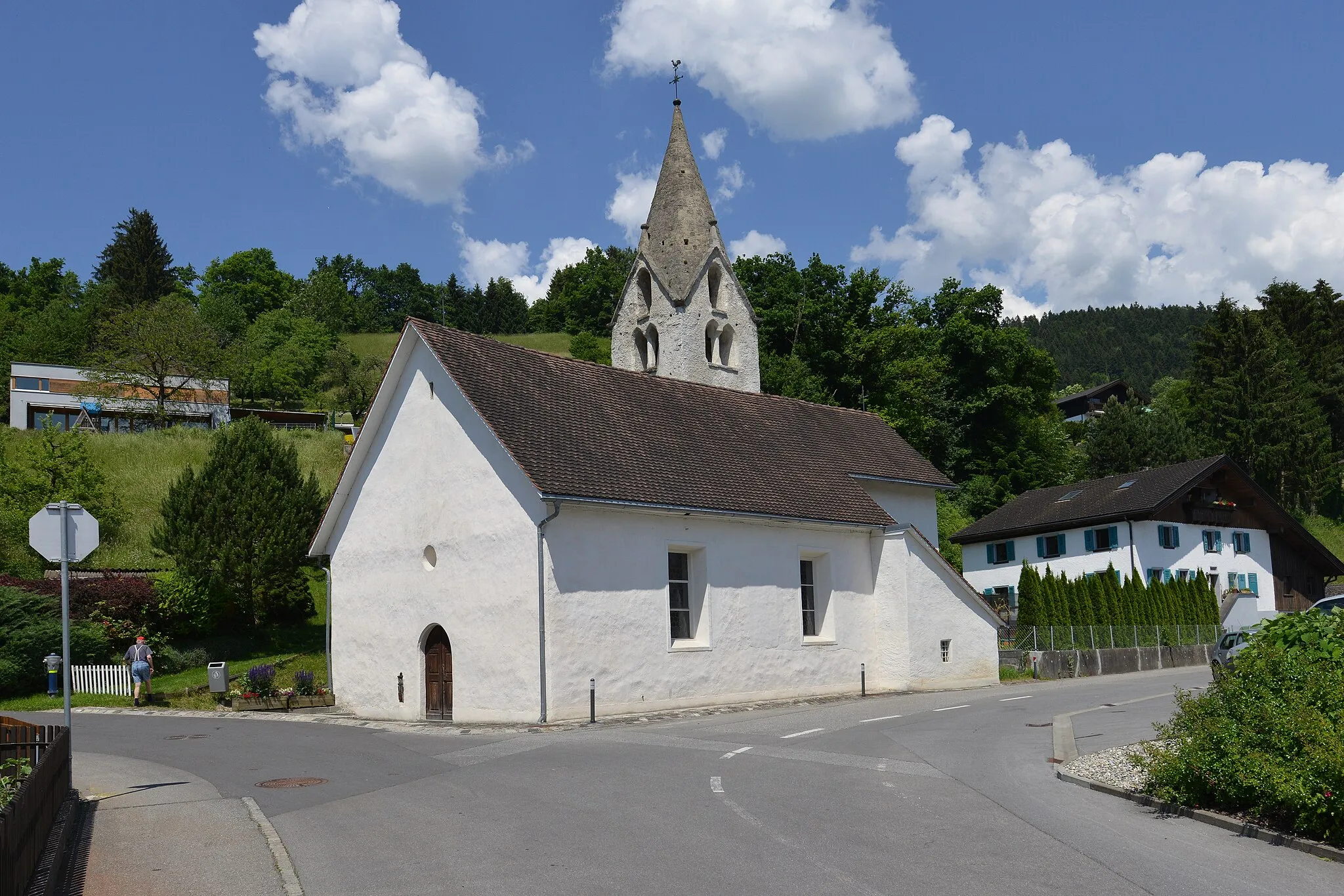 Photo showing: Bludesch, Filialkirche hl. Nikolaus, in Zitz. Urkundlich um 842 "Cise". 1483 Kaplanei. Breiter spätromanischer Bau mit eingezogenem quadratisch barockem Chor unter gemeinsamen Satteldach, Rechteckfenster; Nord-Tur, mit gekoppelten un einfach darüber gestellten Schallöffnungen, vorkragendem Giebelgesims, gemauertem Giebelspitzhelm mit knopfartigen Fialen. Südlich an Langhaus und Chor angebaute Sakristei mit Pultdach von 1629. Im Chor ehemalige Rundapsis durch Ausgrabungen festgestellt, Ummantelung 1629/30.