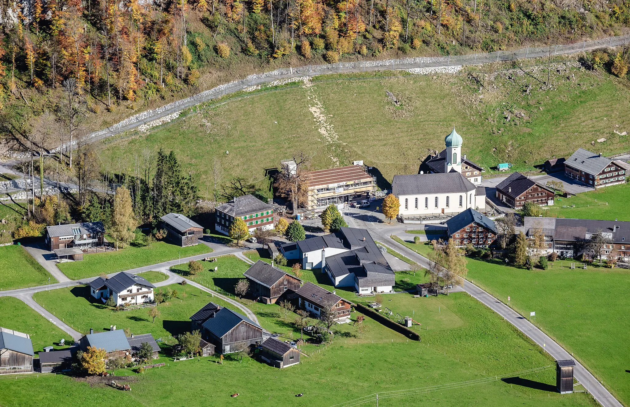 Photo showing: Schrägluftbild vom Gemeindezentrum von Schnepfau mit der Pfarrkirche zum hl. Wolfgang, dem Gemeindeamt, der Volksschule und dem Kindergarten.