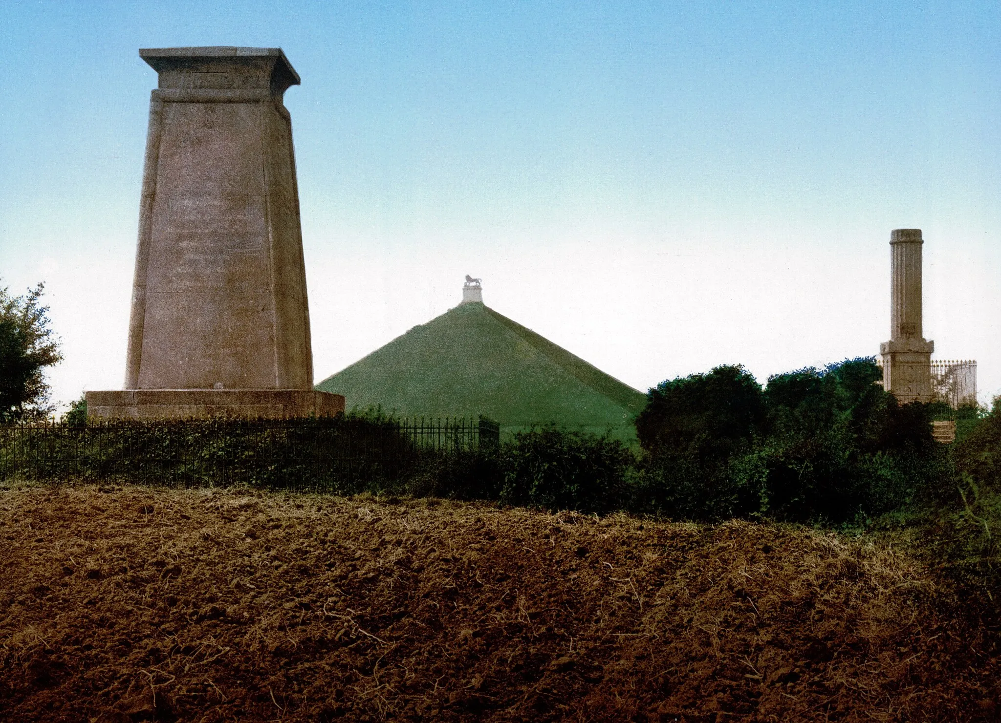 Photo showing: The memorial to the Hanoverians (and the Kings German Legion), the Lion Mound in the distance, and the memorial to Lieutenant-Colonel Sir Alexander Gordon (died 1815) – all on the Waterloo Battlefield.