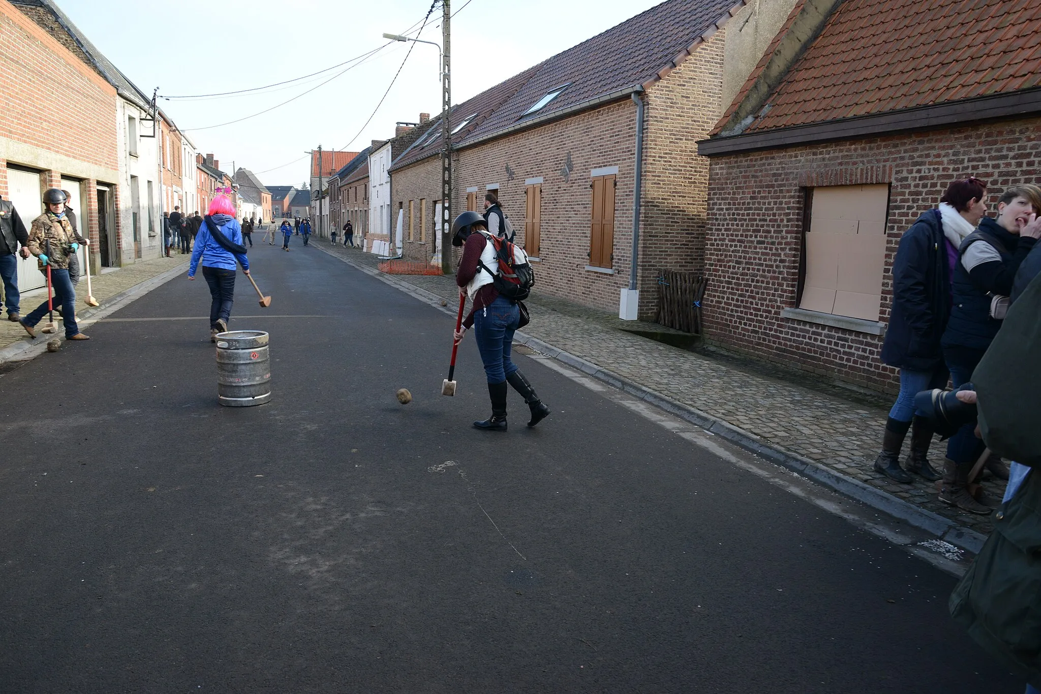 Photo showing: U.S. Air Force Master Sgt. Darcy Babutzke, NATO Communications and Information Agency, Supreme Headquarters Allied Powers in Europe (SHAPE), is about to finish off a game as she participates in traditional a festivity in the town of Chièvres, Belgium, Feb. 18, 2015. This annual golf-like, medieval sport of “crossage," takes place the day after Mardi Gras. Players drive a oak ball, called a “chôlette” (pronounced: show-let), with a wooden club, or “rabot” (pronounced: rah-bo), into metal kegs targets set up around town. Whenever a player is ready to swing, he yells: “Chôlette.”(U.S. Army photo by Visual Information Specialist Henri Cambier/Released)
