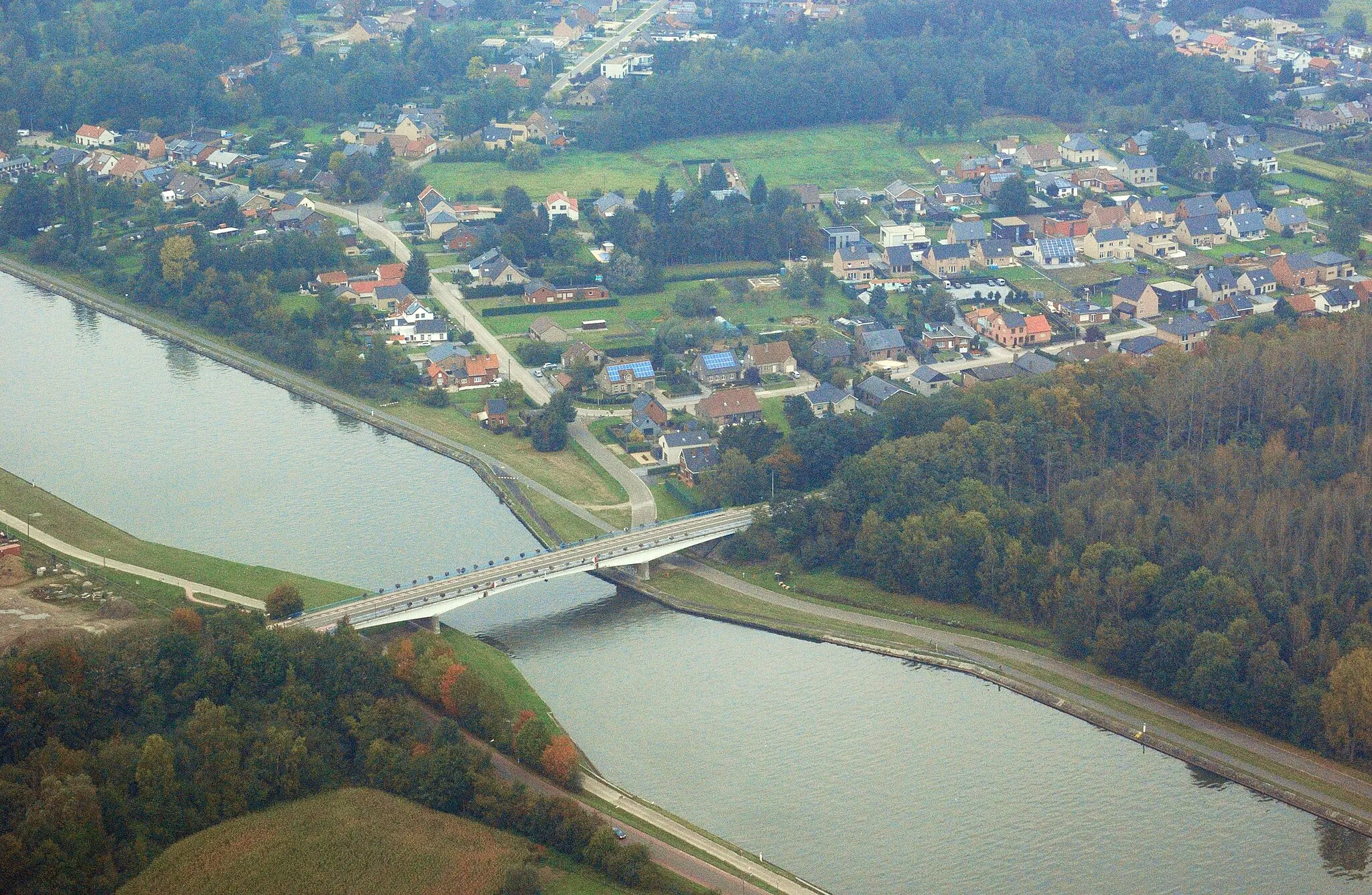 Photo showing: The village of Stokrooie in the Belgian municipality of Hasselt is cut in two by the Albert Canal. This photograph offers an aerial view of the northern half of Stokrooie, viewed from the south-southeast. Nikon D60 f=55mm f/9 at 1/320s ISO 800. Contrast and colours enhanced using Nikon NX Studio 1.3.2. Framed using GIMP 2.10.34.