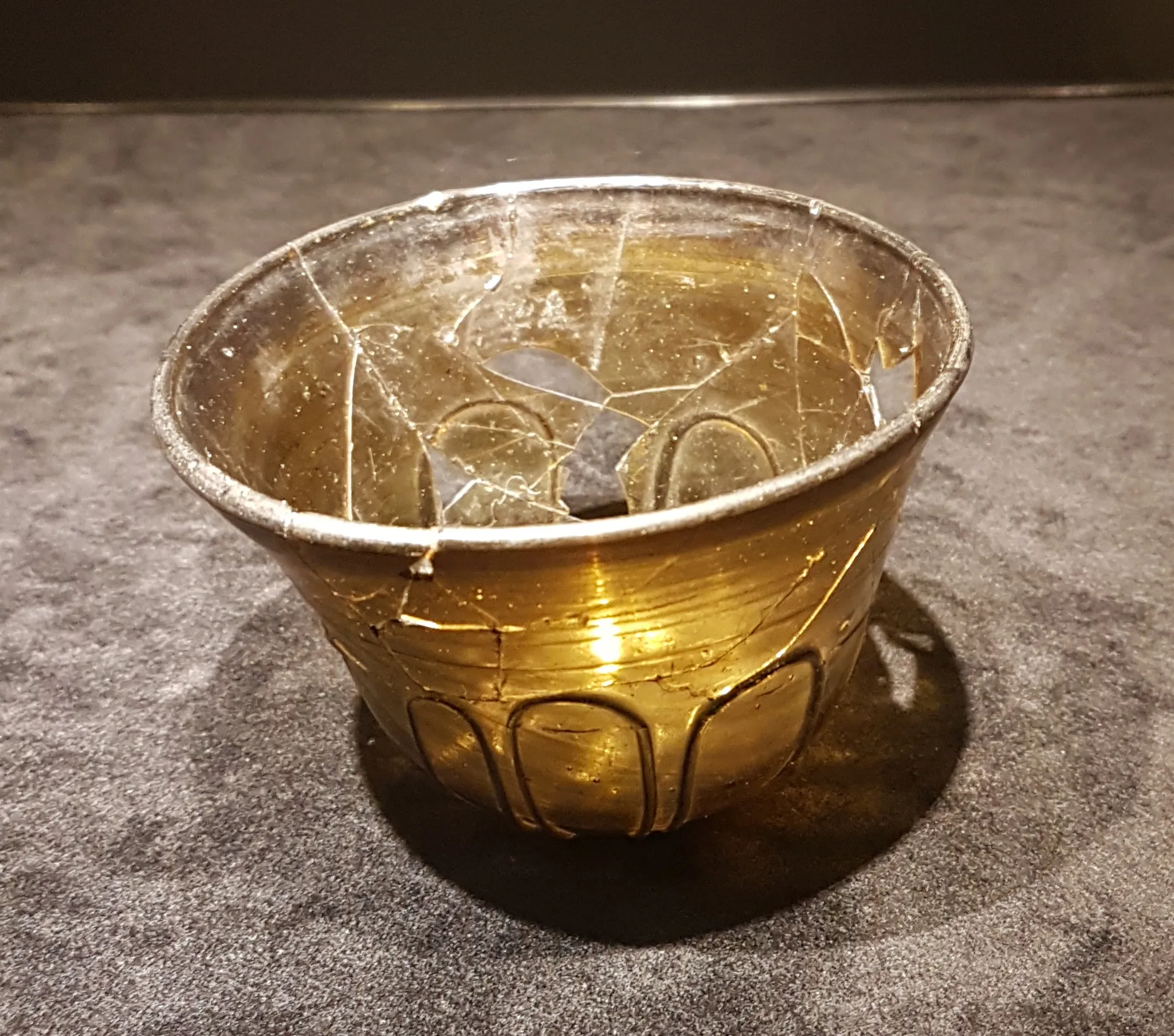 Photo showing: Merovingian glass palm cup found in 1969 in a woman's grave at Diepstraat, Rosmeer, Belgium (near Tongeren). Hight: 6.8 cm. The glass can be dated between 550 and 630 AD (the grave also contained a gold coin of 610-620 AD). Archaeological collection of Gallo-Romeins Museum Tongeren. Photographed at the temporary exhibition Top or Topic in Centre Céramique in Maastricht, the Netherlands.