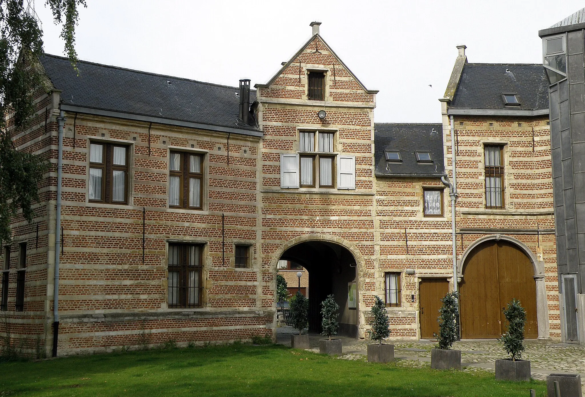 Photo showing: Anvers, Belgique. Château et manoir de plaisance dit Bisschoppenhof, complexe de bâtiments contigus, sis Suzanne Spanhovenstraat à Deurne-Nord, dans la banlieue nord-est d’Anvers, sur le bord d’un terrain circulaire arboré et entouré d’une douve. Le complexe comprend : une porterie du XVIe siècle, auquel donne accès un pont à arche ; attenant à celle-ci, sur son côté gauche, le corps de logis principal, daté du XVIIe, mais remanié (not. les baies et le perron) fin XIXe ; contigu à ce dernier, un autre corps de logis, extension datant du début XIXe. Photographie montrant la façade arrière (c.-à-d. est) de la porterie.