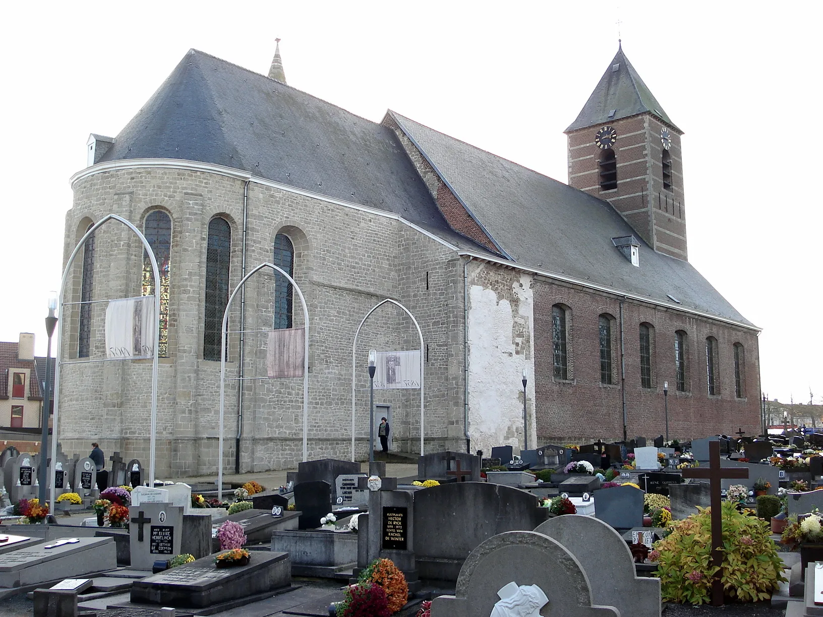 Photo showing: Sint-Lievens-Houtem, Oost-Vlaanderen, België. Sint-Michielskerk, noordergevel, met: bakstenen classicistisch schip (1776) en klokkentoren; zandstenen romaans koor (11e de 12e eeuw). Van het noordelijk flankeertorentje blijft enkel de onderbouw over (witte pleister); zuidelijk flankeertorentje steekt nog net boven dak van koor uit.