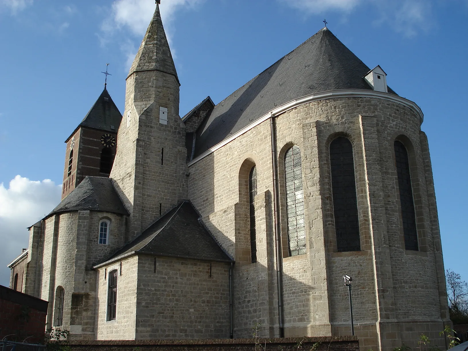 Photo showing: Sint-Lievens-Houtem, België (Oost-Vlaanderen). Sint-Michielskerk, met: romaans koor, flankeertoren, kapel (helemaal links op foto), uit 11e en 12e eeuw. In hoek tussen koor en kapel: sacristie, 18e eeuw. Verder: bakstenen klokkentoren en (amper zichtbaar) bakstenen schip, classicistisch, 1776.