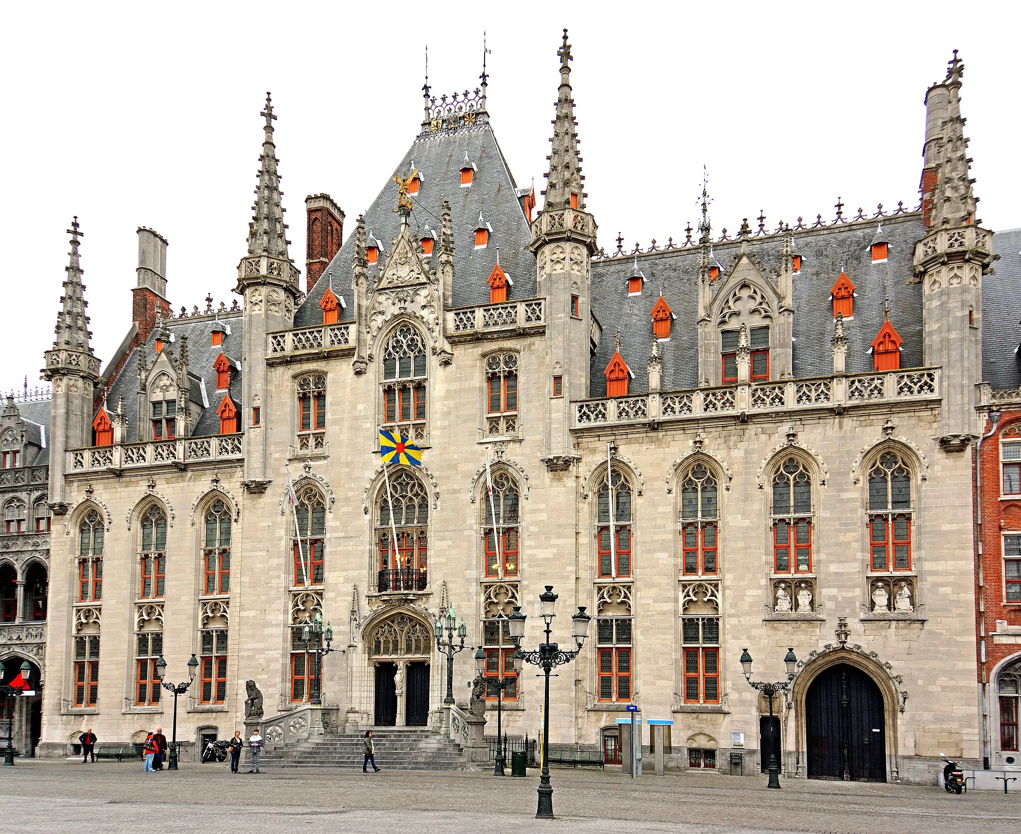 Photo showing: PLEASE, NO invitations or self promotions, THEY WILL BE DELETED. My photos are FREE to use, just give me credit and it would be nice if you let me know, thanks.
The Provincial Court is the best example of how Bruges was renovated in neo-gothic style during the second half of the 19th century. After the destruction of the water halls in 1787 a new complex of houses was built in classicist style. This style was considered very modern in a town that was basically built in late-gothic style. In 1850 the provincial government bought the complex, enlarged it and made it the seat of the provincial institutions. The members of the catholic and traditionalist political parties rejected the building as 'unfit for the beautiful gothic Bruges'. In 1878 a fire destroyed most of the building. Different groups took their chance to have it reconstructed in neo-gothic style, the 'house'-style of the catholic party. On the left side of the complex is now the house of the Governor of the Province of West-Flanders. The red brick building on the right side is the Post Office of Bruges.