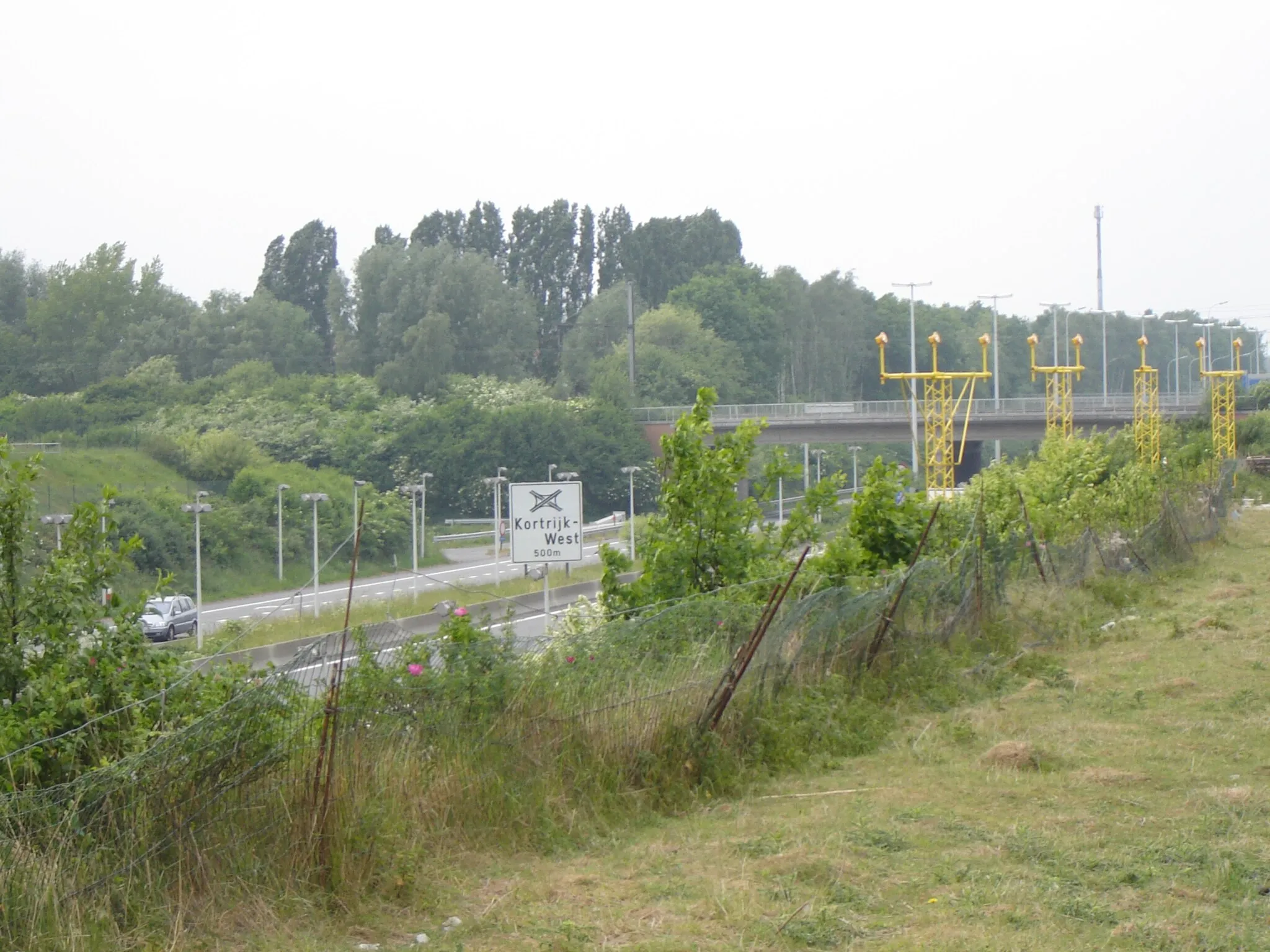 Photo showing: Ringway of Kortrijk R8, in Bissegem, between exit Bissegem and intersection Kortrijk-West (A19). Road as at the end of the landing strip of the airport of Kortrijk-Wevelgem, hence the low lamp posts for the road, and light signals for the landing strip. Bissegem, Kortrijk, West Flanders, Belgium