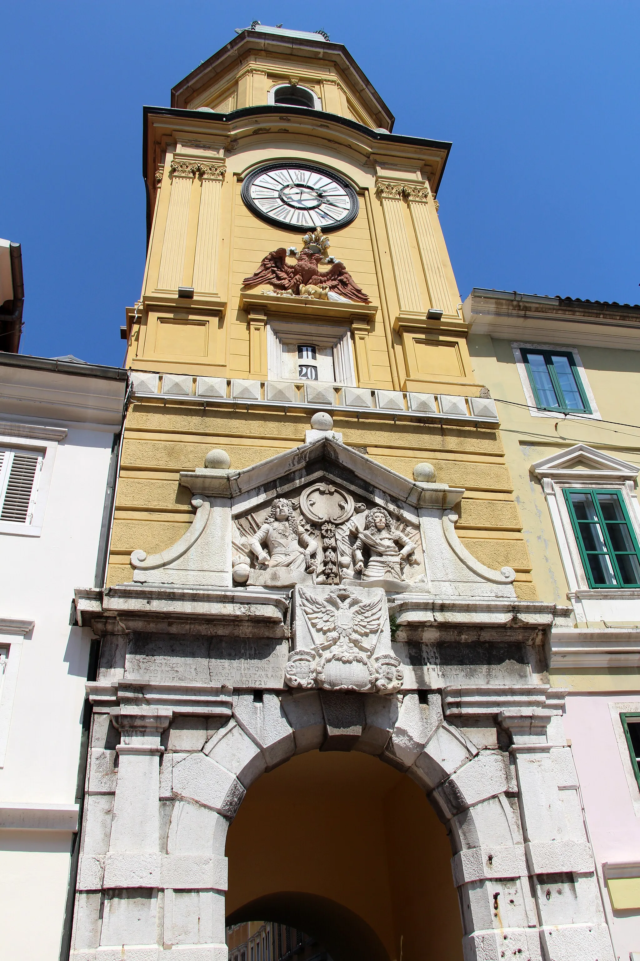 Photo showing: Luka - Korzo

City Clock Tower was built in the Middle Ages, probably on the foundations of the Late Antique littoral town gates. Some baroque phases of its construction can be seen on the lower part of the front of the Tower, which are characterised by a richly decorated portal, an imperial coat of arms carved out of stone and a relief of the Austrian emperors Leopold and Charles VI.