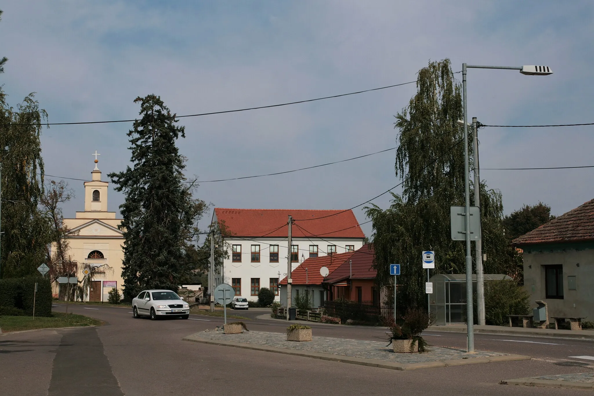 Photo showing: Obec Pravice v okrese Znojmo. Autobusová zastávka při hlavní silnici v centru obce, v pozadí kostel Nejsvětější Trojice a obecní úřad.