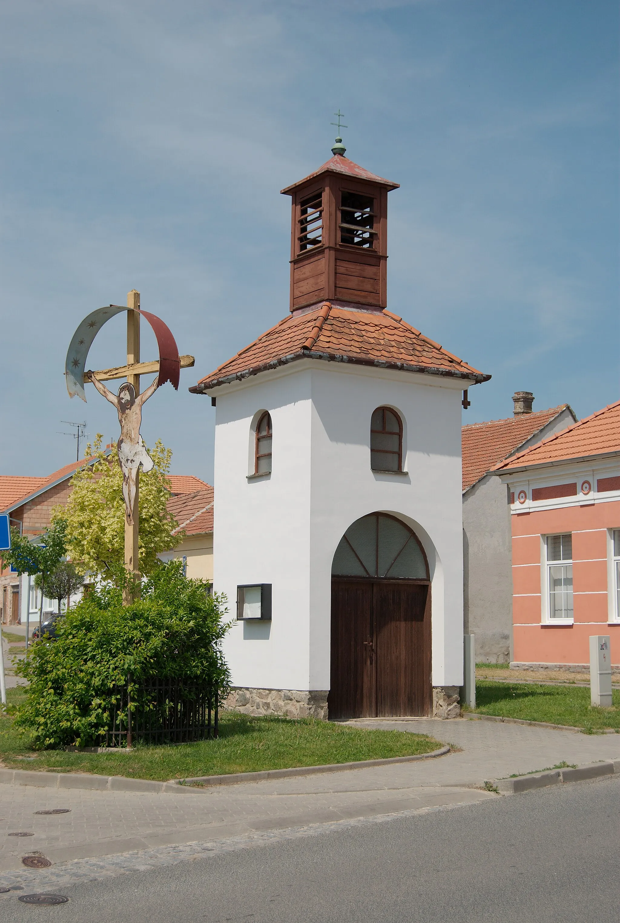 Photo showing: Brno-Jehnice - zvonice na náměstí 3. května, postavená roku 1968. Kříž vedle ní je z roku 1965.