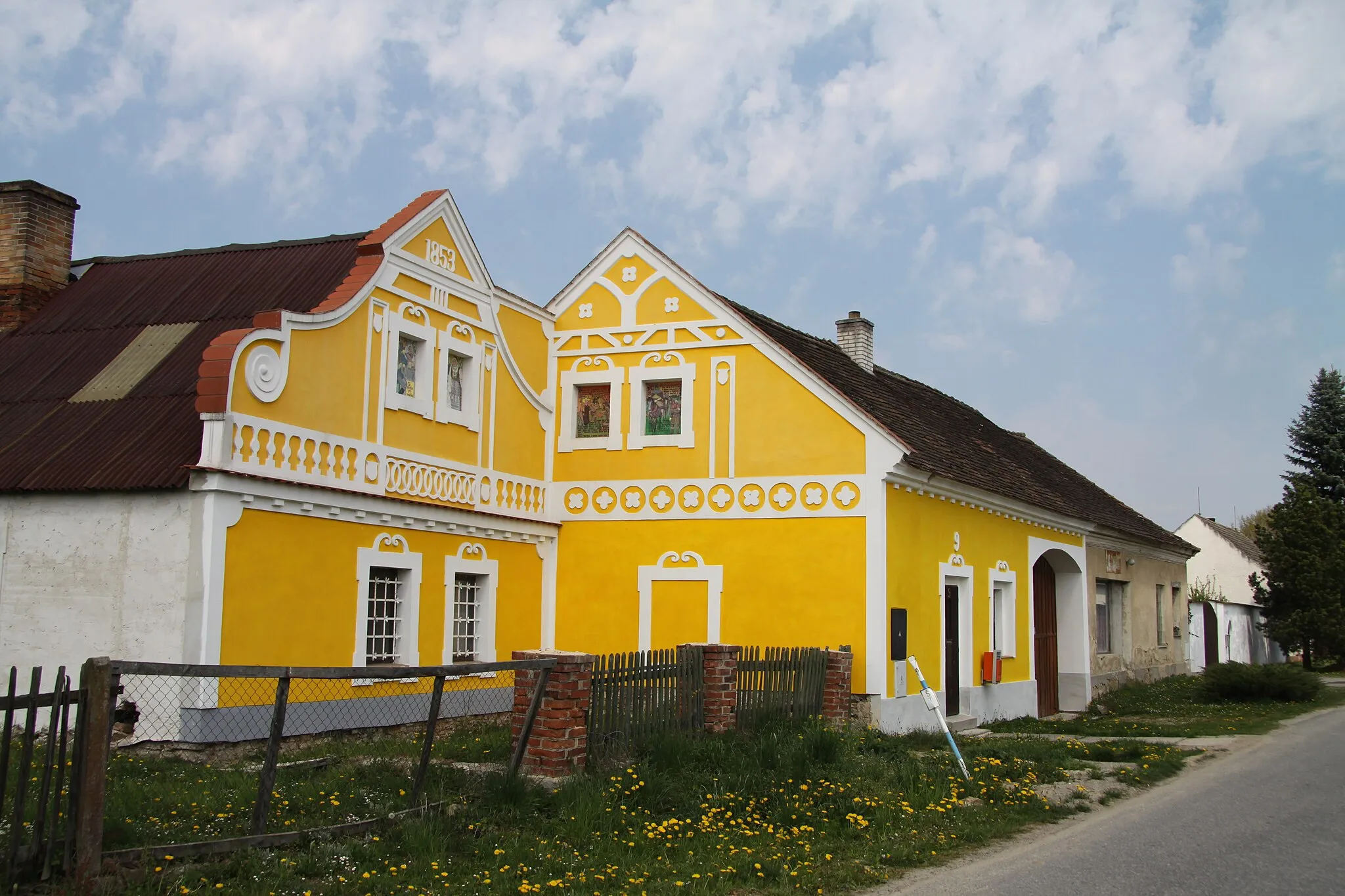 Photo showing: A traditional farmhouse in Radomilice, South Bohemian Region, Czech Republic. According to the owner, the left-hand part was built in 1853 - as written on the gable - while the right-hand part is more recent. The house has been recently renovated and false windows on the top decorated with replicas of 19th century paintings, Radomilice, České Budějovice District, Czech Republic